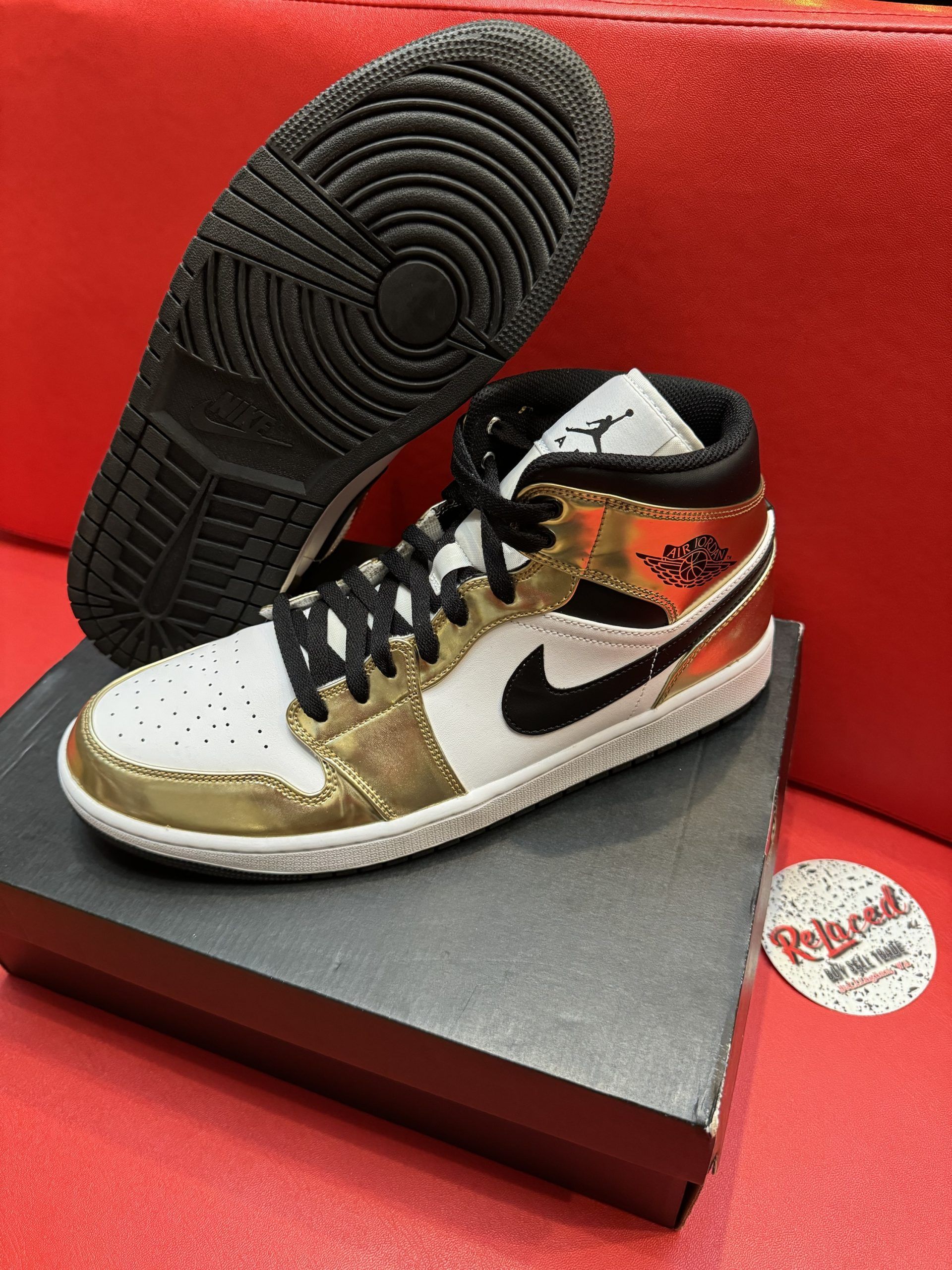 White, gold, and black Air Jordan 1 Mid sneaker on black box; black sole visible.
