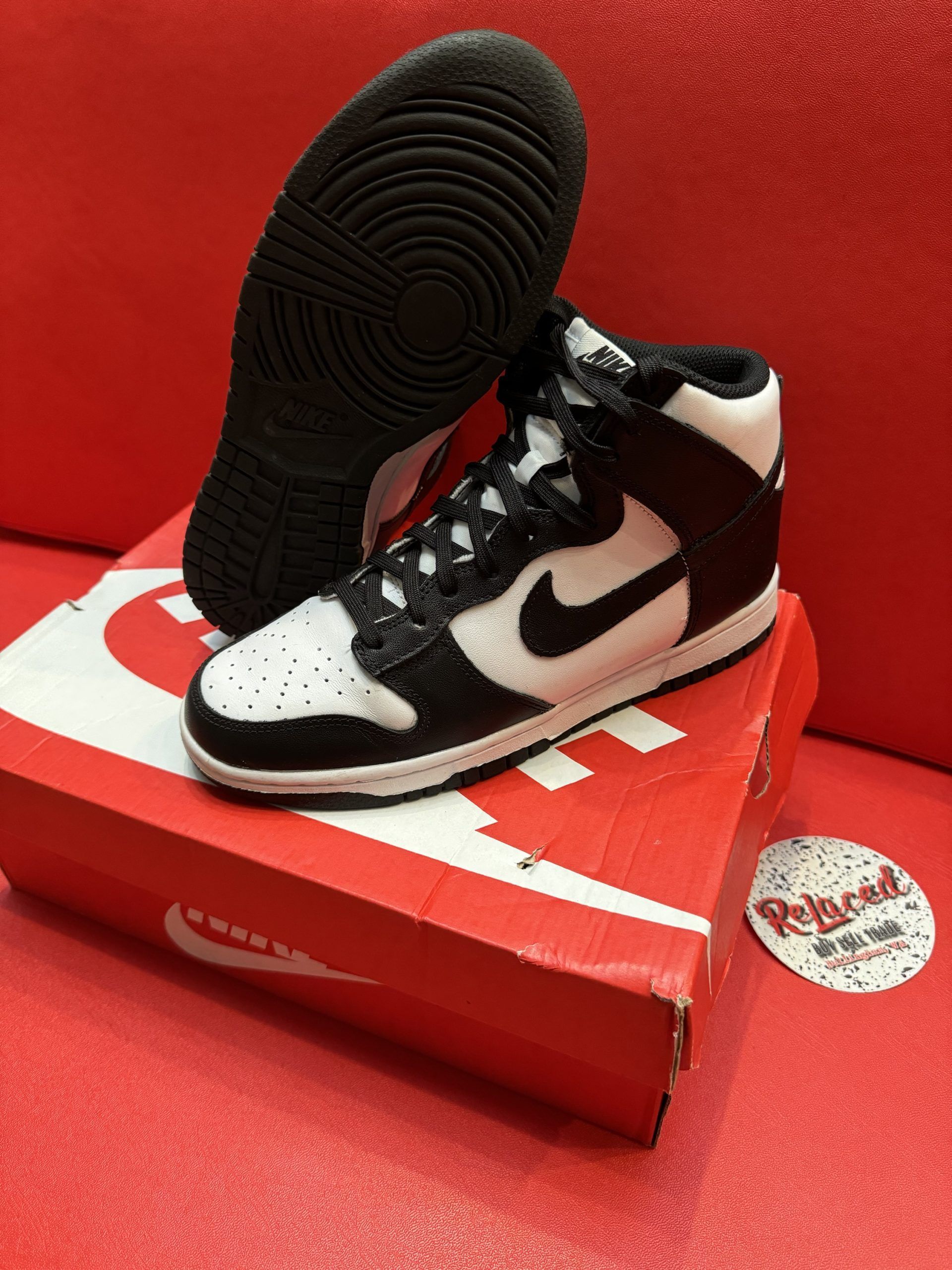 Black and white Nike Dunk High sneakers on a red box and red background.
