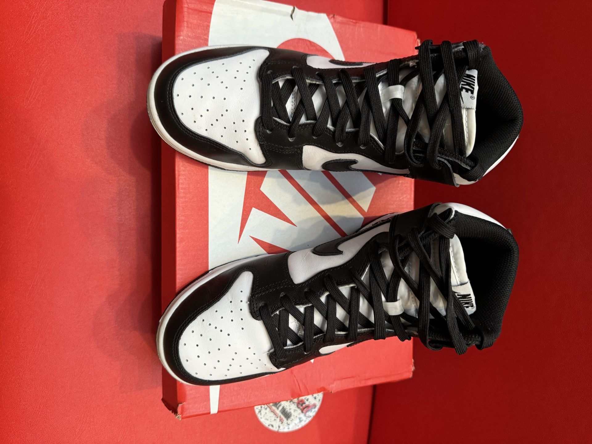 Black and white Nike Dunk High sneakers on a red box and red background.