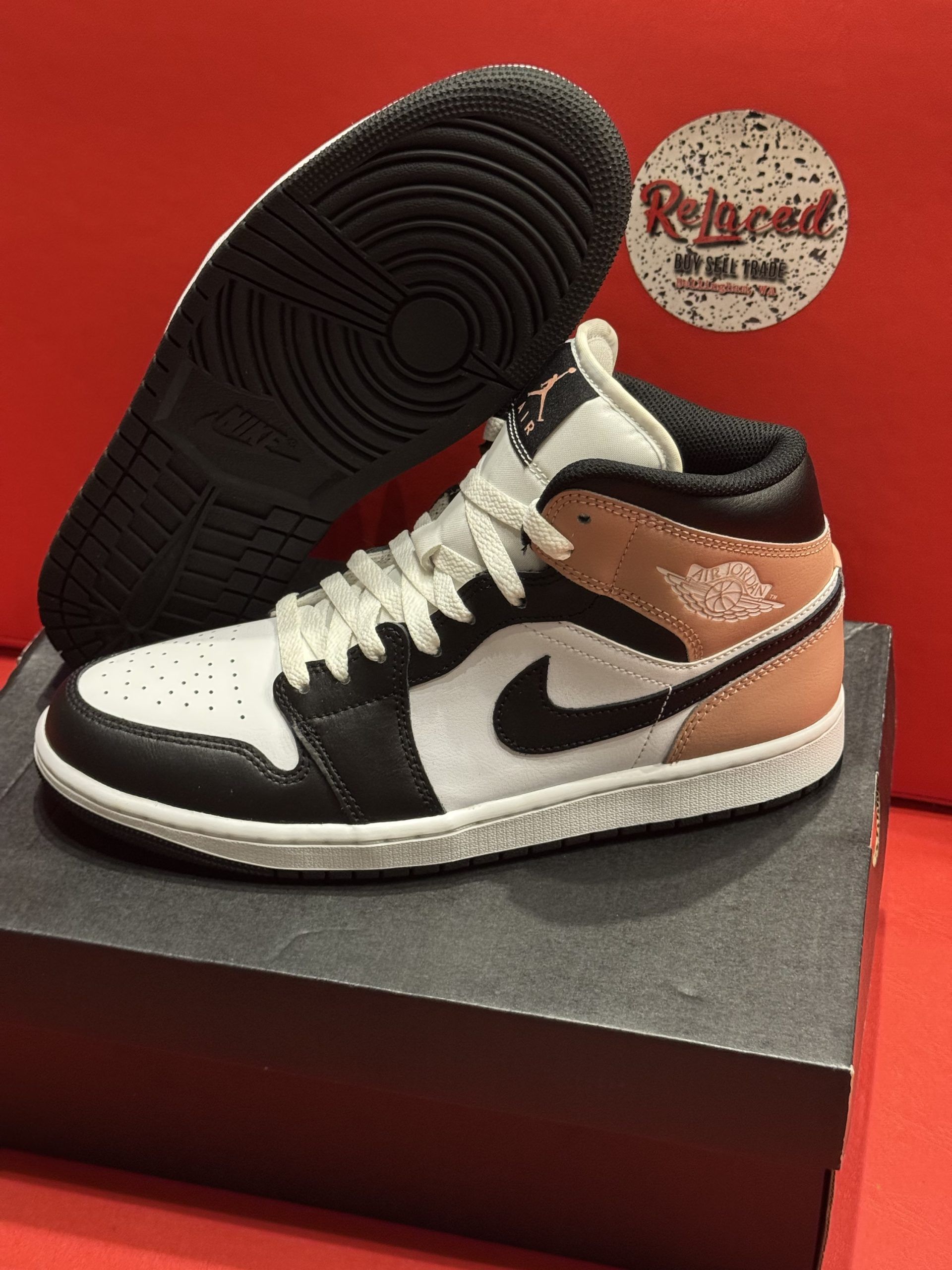 Air Jordan 1 Mid sneaker with a black, white, and tan color scheme, sitting on a black box, with the sole visible.