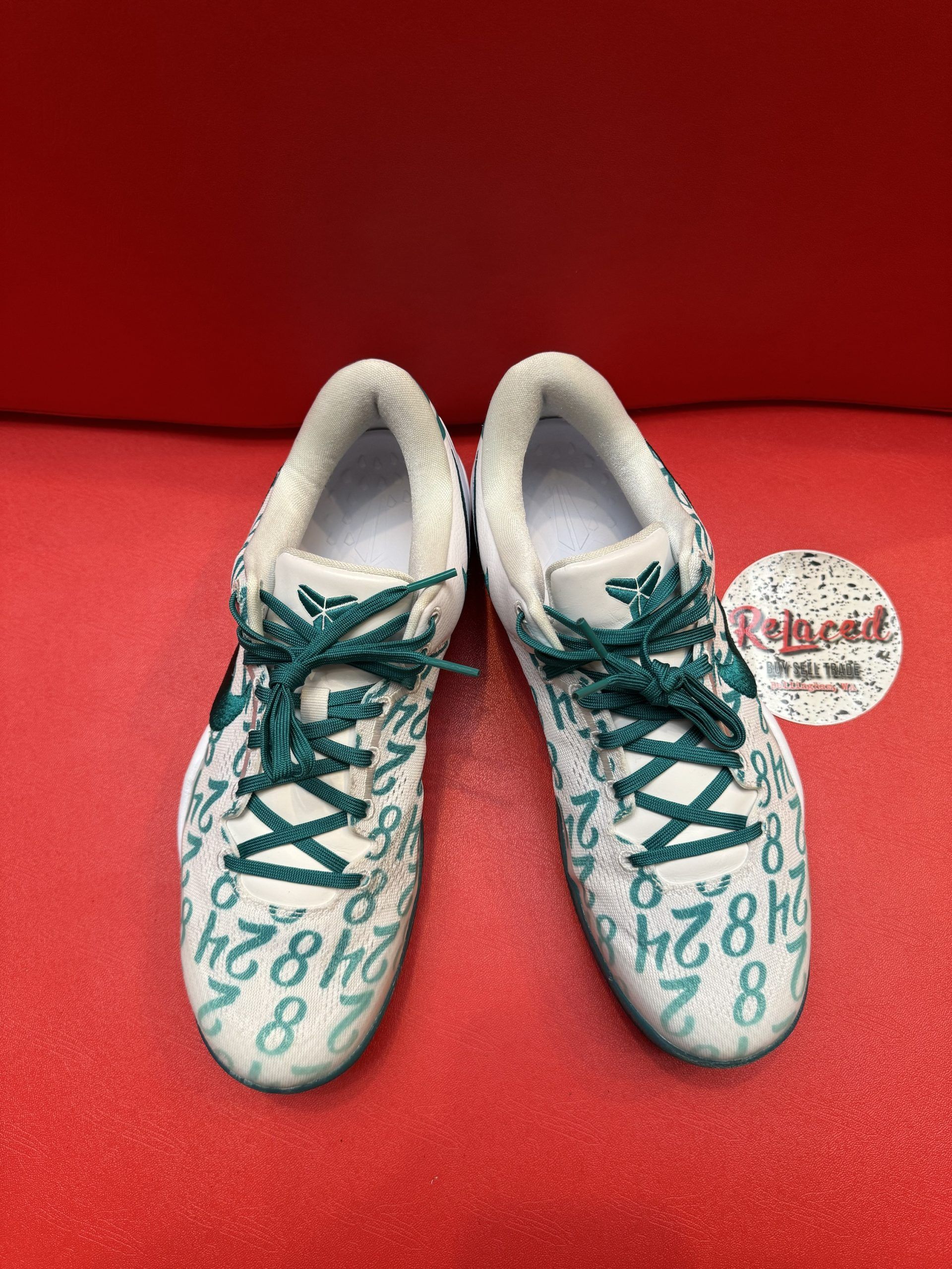 White and teal Nike basketball shoe with teal sole, number details, on a red surface.