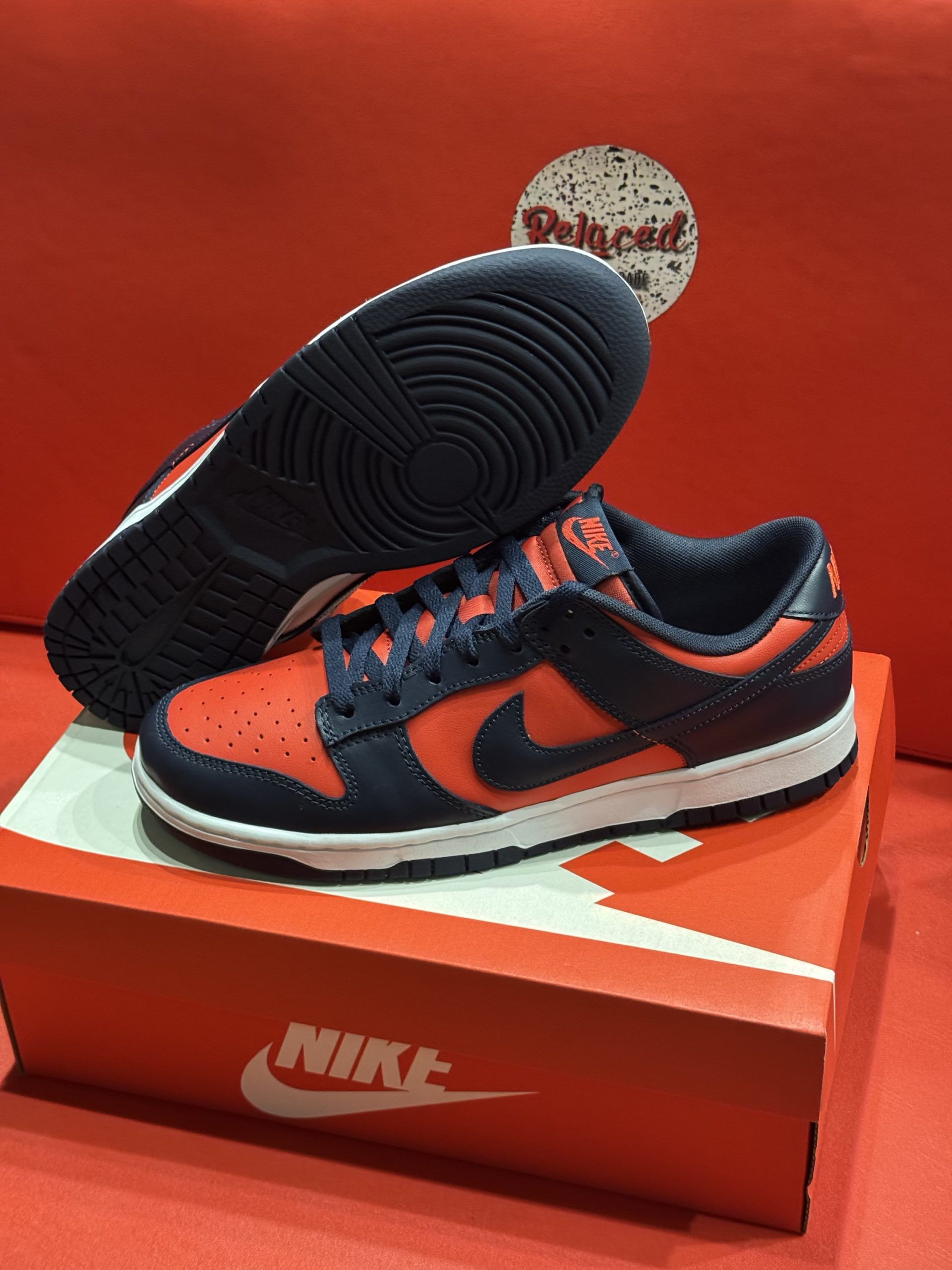 Nike Dunk Low sneakers, orange and navy blue, on top of an orange Nike shoebox against a red background.