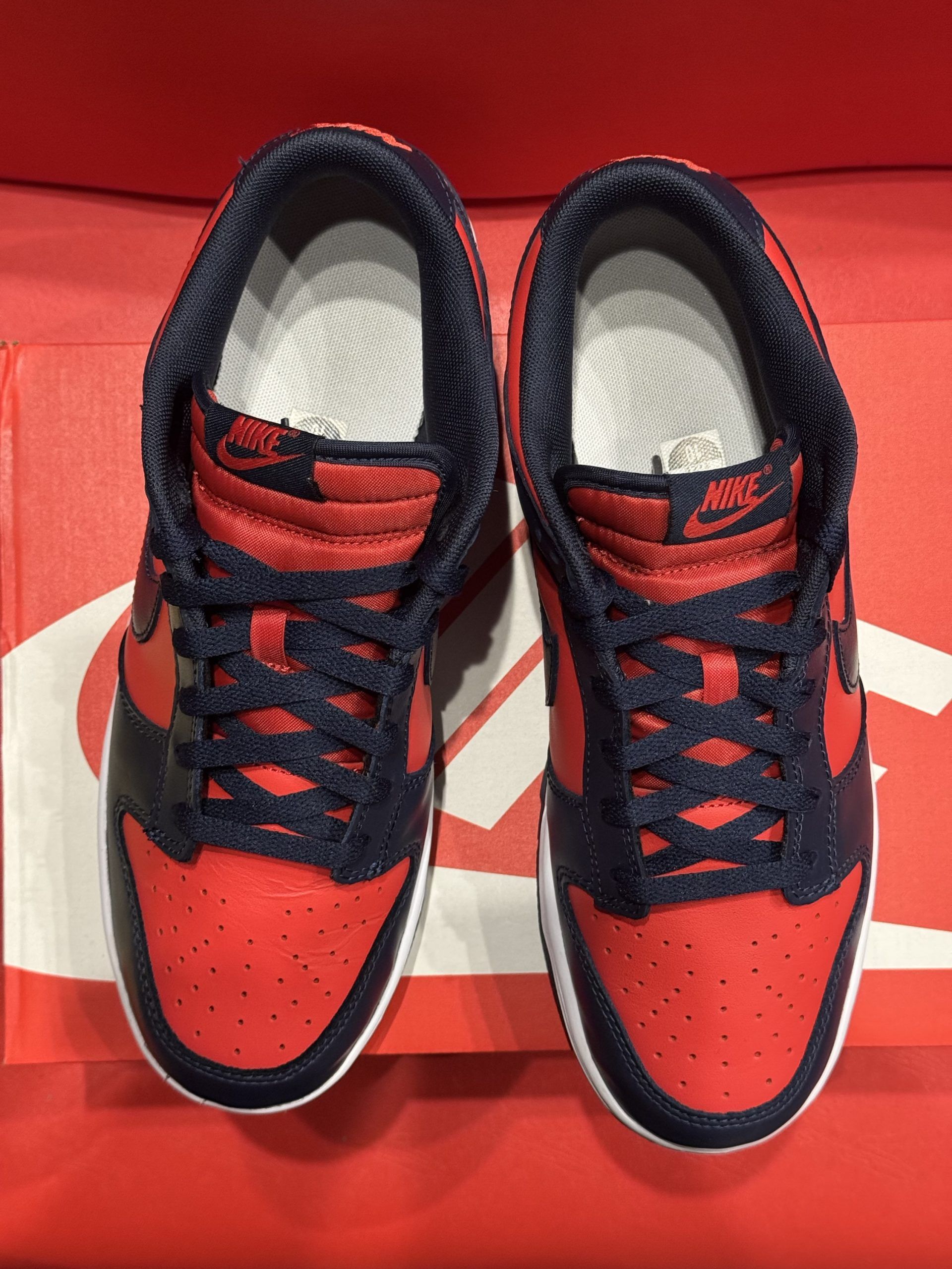 Nike Dunk Low sneakers, orange and navy blue, on top of an orange Nike shoebox against a red background.