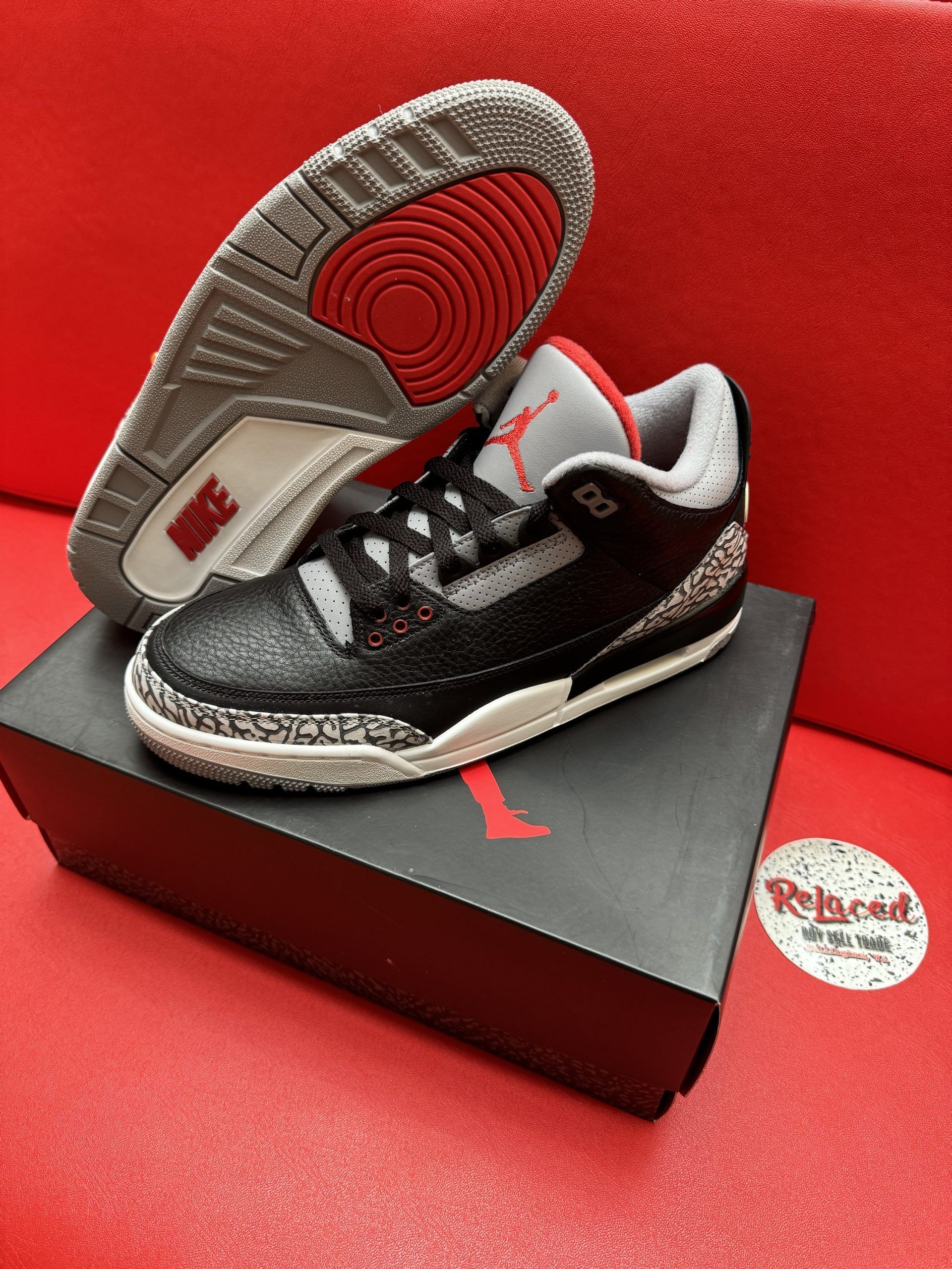 Air Jordan 3 black sneakers with elephant print, sitting on a black box, red background.