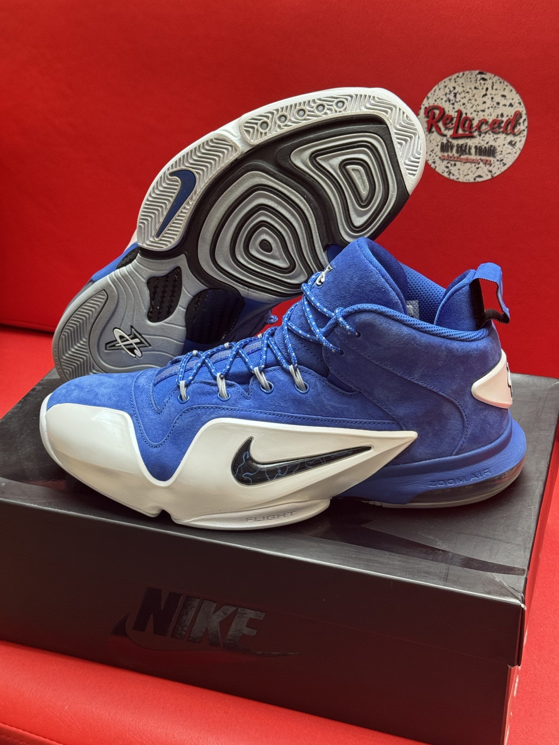 Blue and white Nike basketball shoes with a black Nike box and red background.