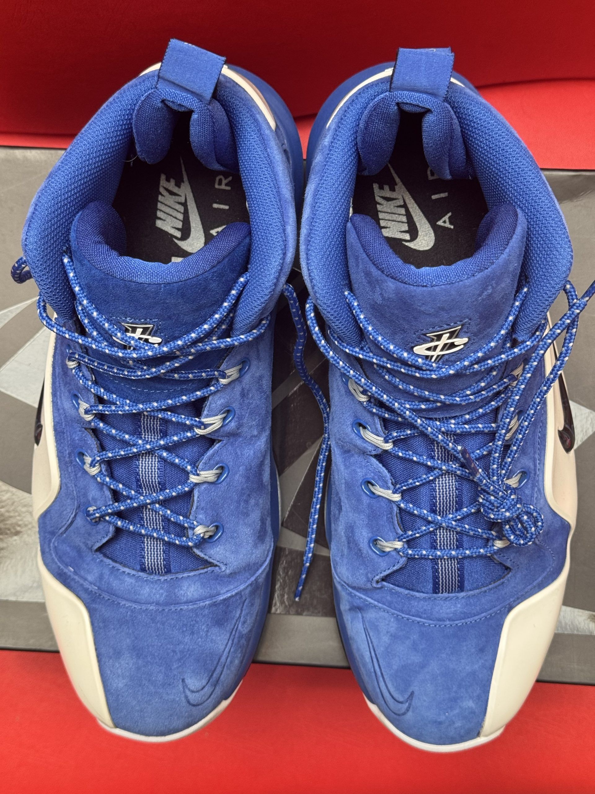 Blue and white Nike basketball shoes with a black Nike box and red background.