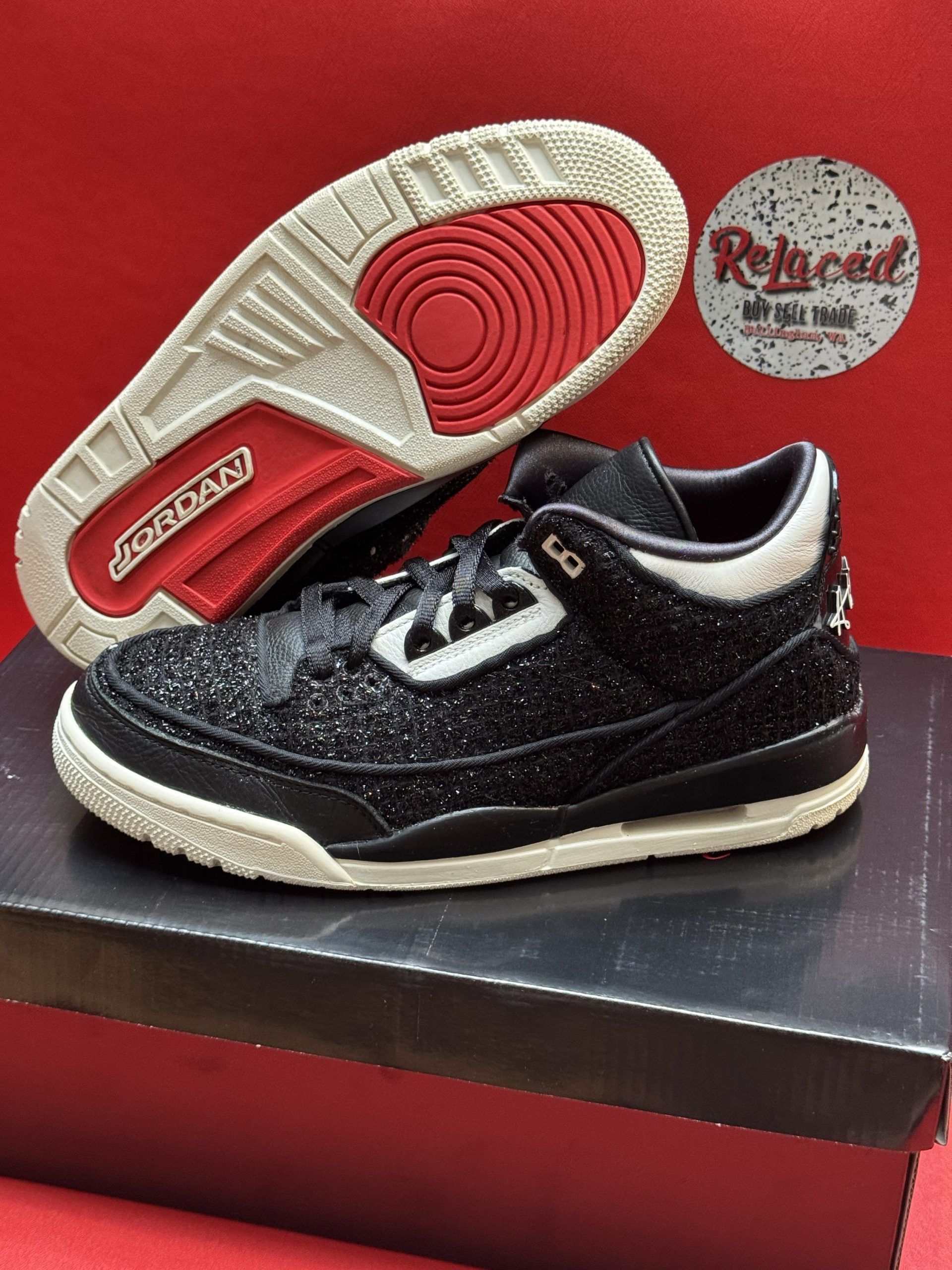 Black and white Jordan 3 sneakers with glitter overlay, sitting on a black shoebox, sole visible.