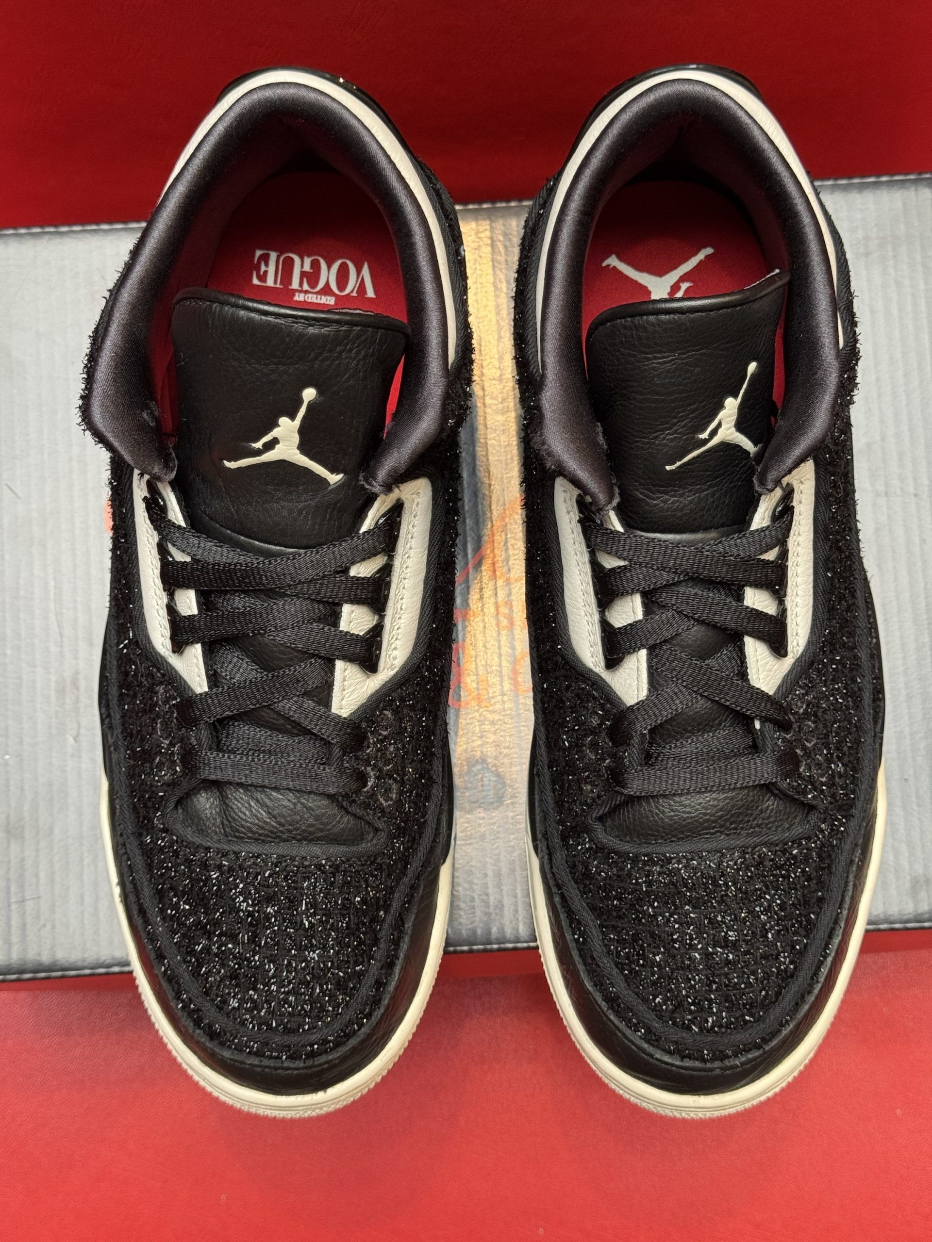 Black and white Jordan 3 sneakers with glitter overlay, sitting on a black shoebox, sole visible.
