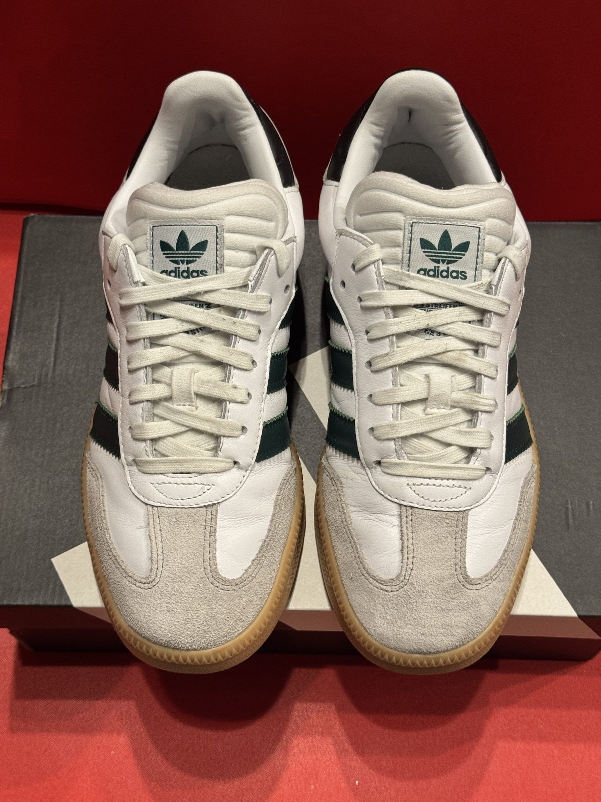 Adidas Samba sneakers with green stripes and gum sole, atop a shoebox, with one shoe’s sole displayed.