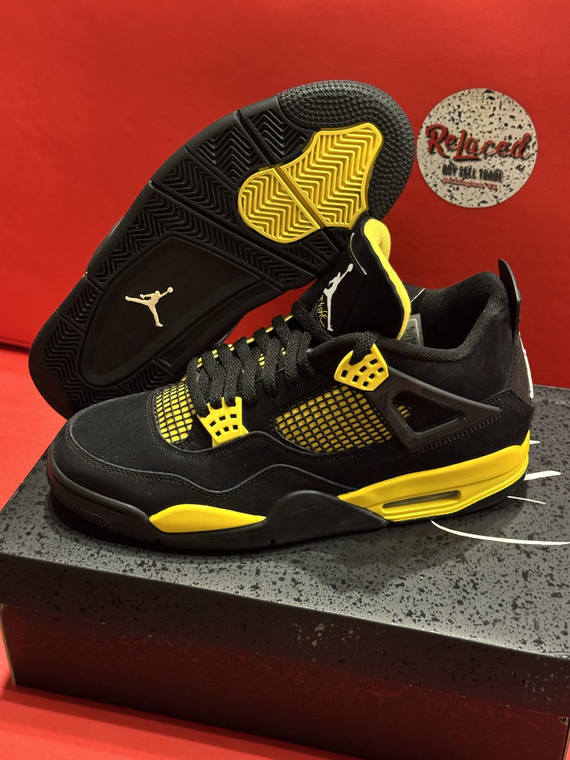 Black and yellow Air Jordan 4 sneakers on a black shoe box, with the sole visible.