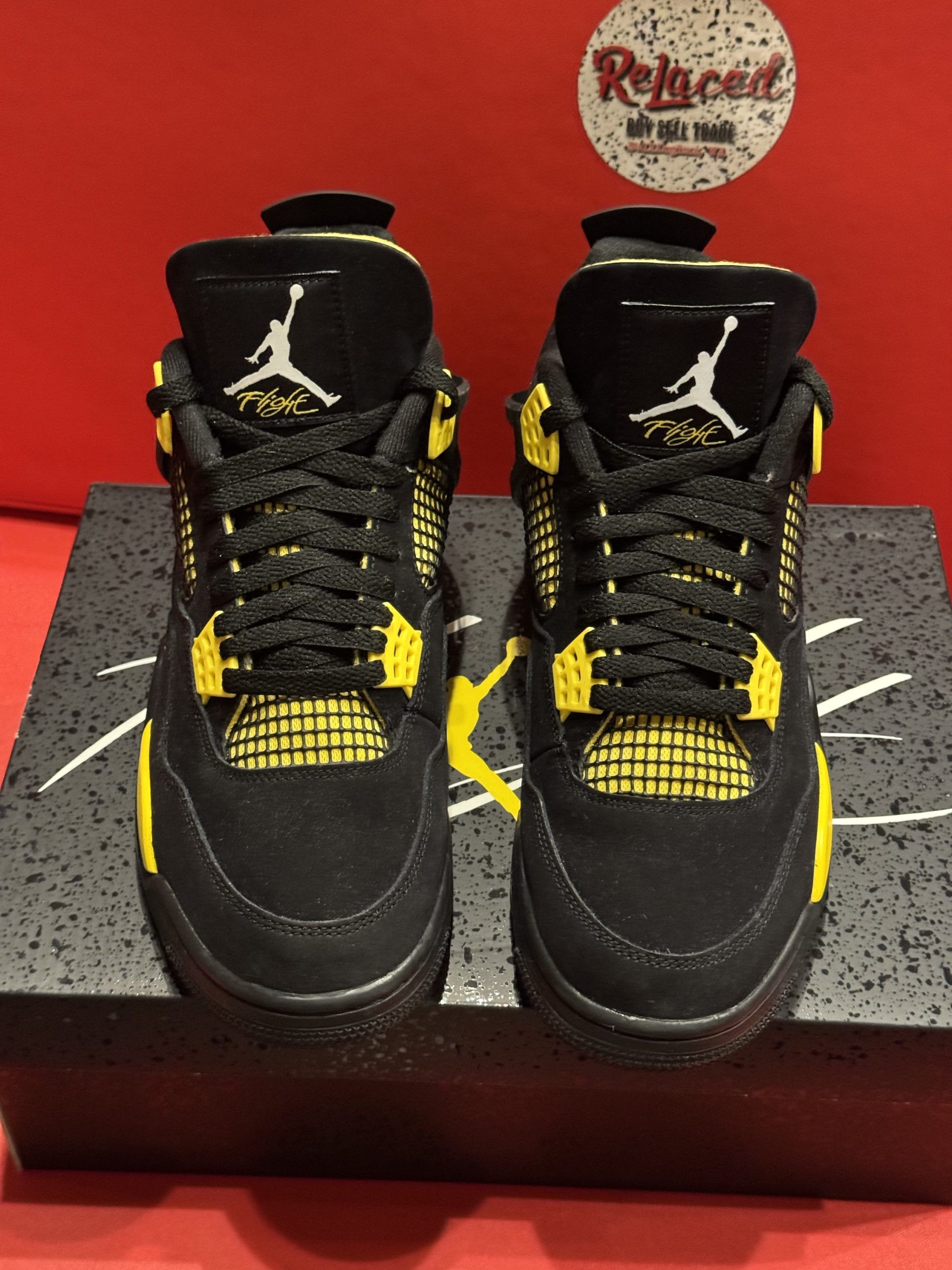 Black and yellow Air Jordan 4 sneakers on a black shoe box, with the sole visible.