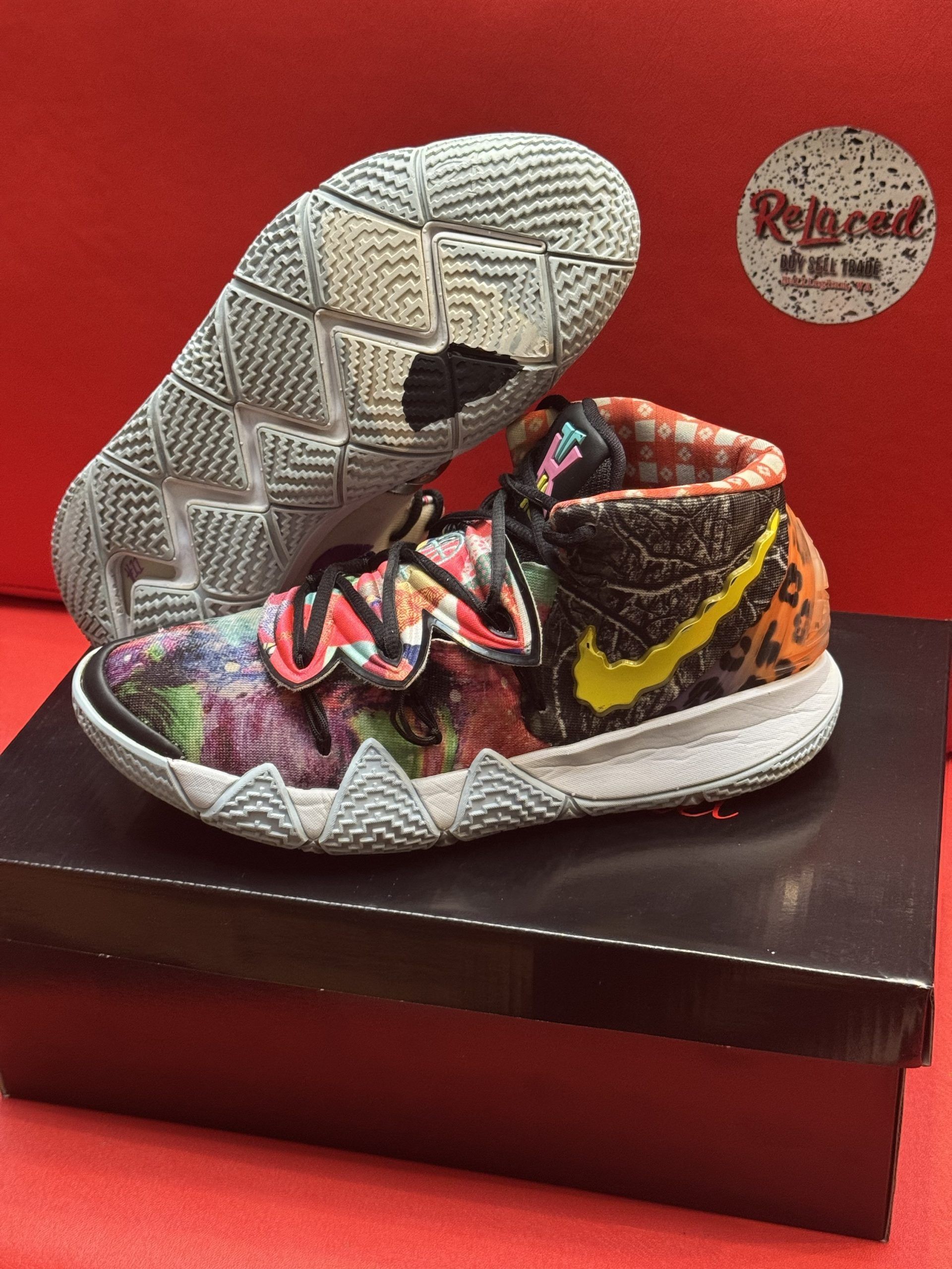 Colorful Nike Kyrie sneakers on a black box, with the sole visible. Red background, brand logo present.
