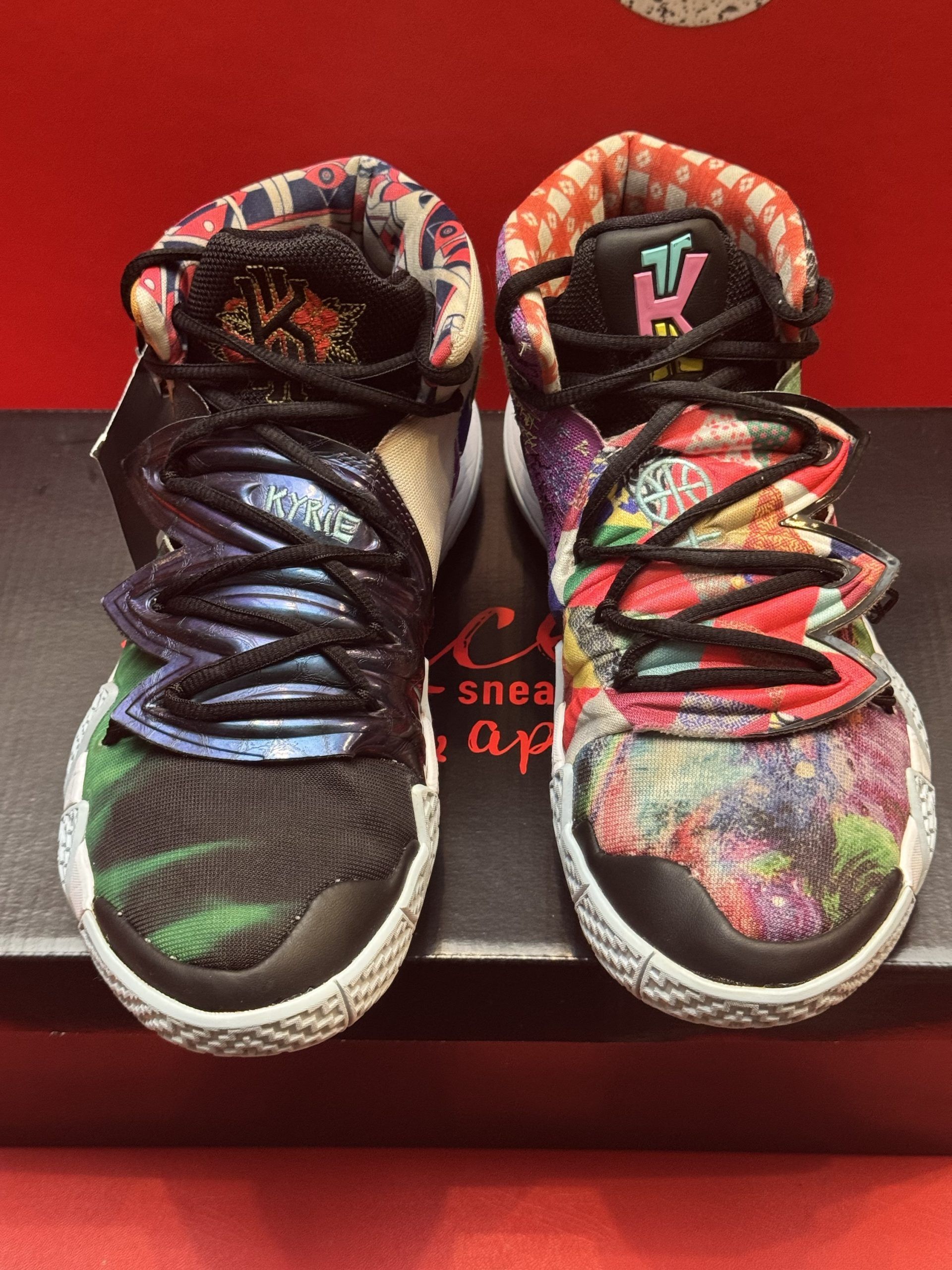 Colorful Nike Kyrie sneakers on a black box, with the sole visible. Red background, brand logo present.