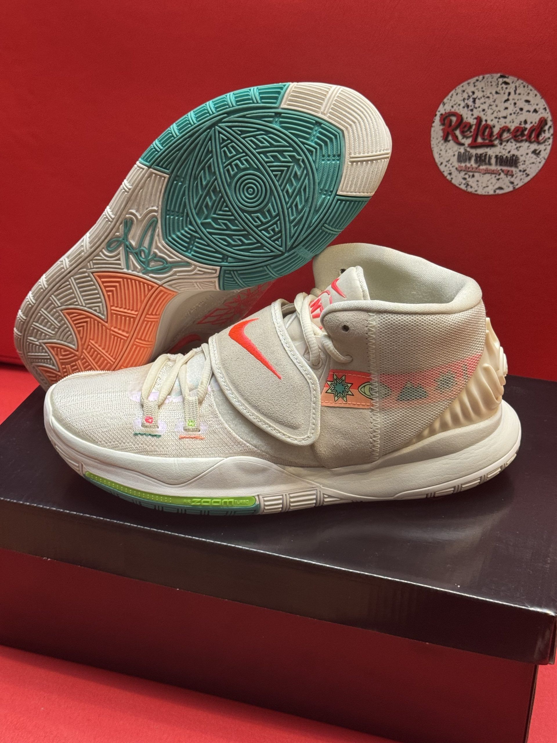 White, beige, and orange Kyrie basketball shoe on a box, sole up showing teal and orange accents.