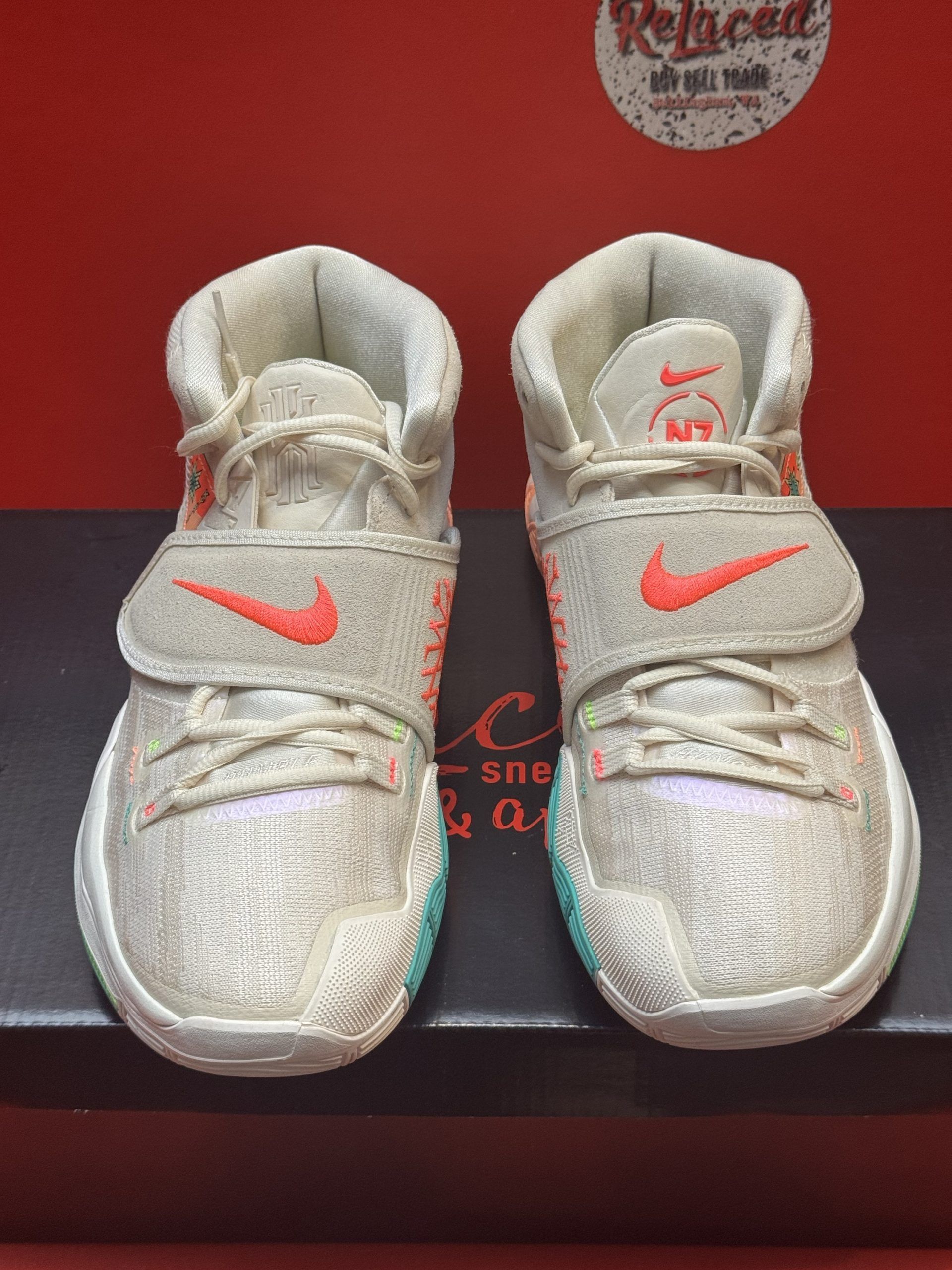 White, beige, and orange Kyrie basketball shoe on a box, sole up showing teal and orange accents.