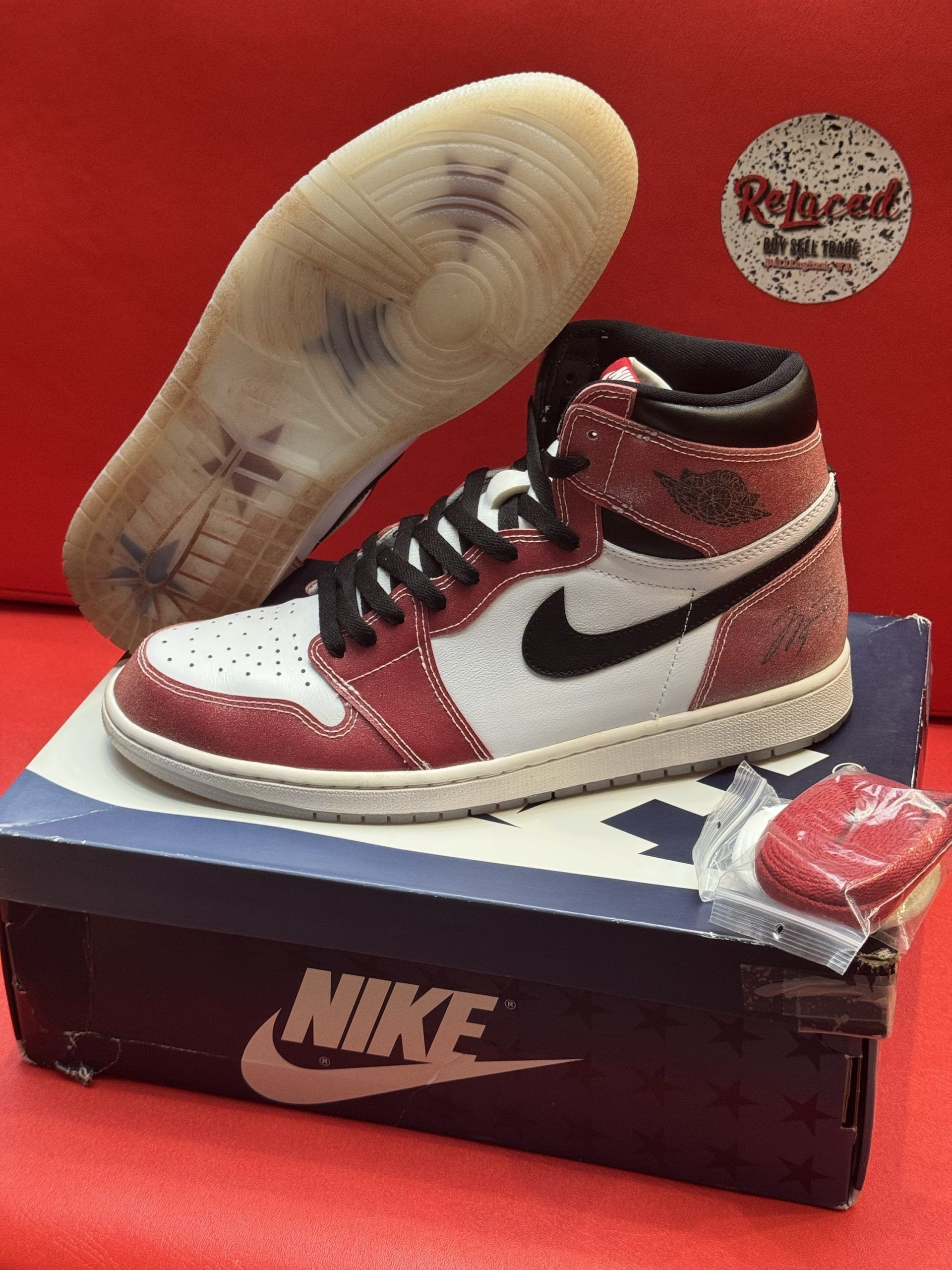 Air Jordan 1 sneaker with white, red, and black accents, sitting on a blue Nike shoebox.