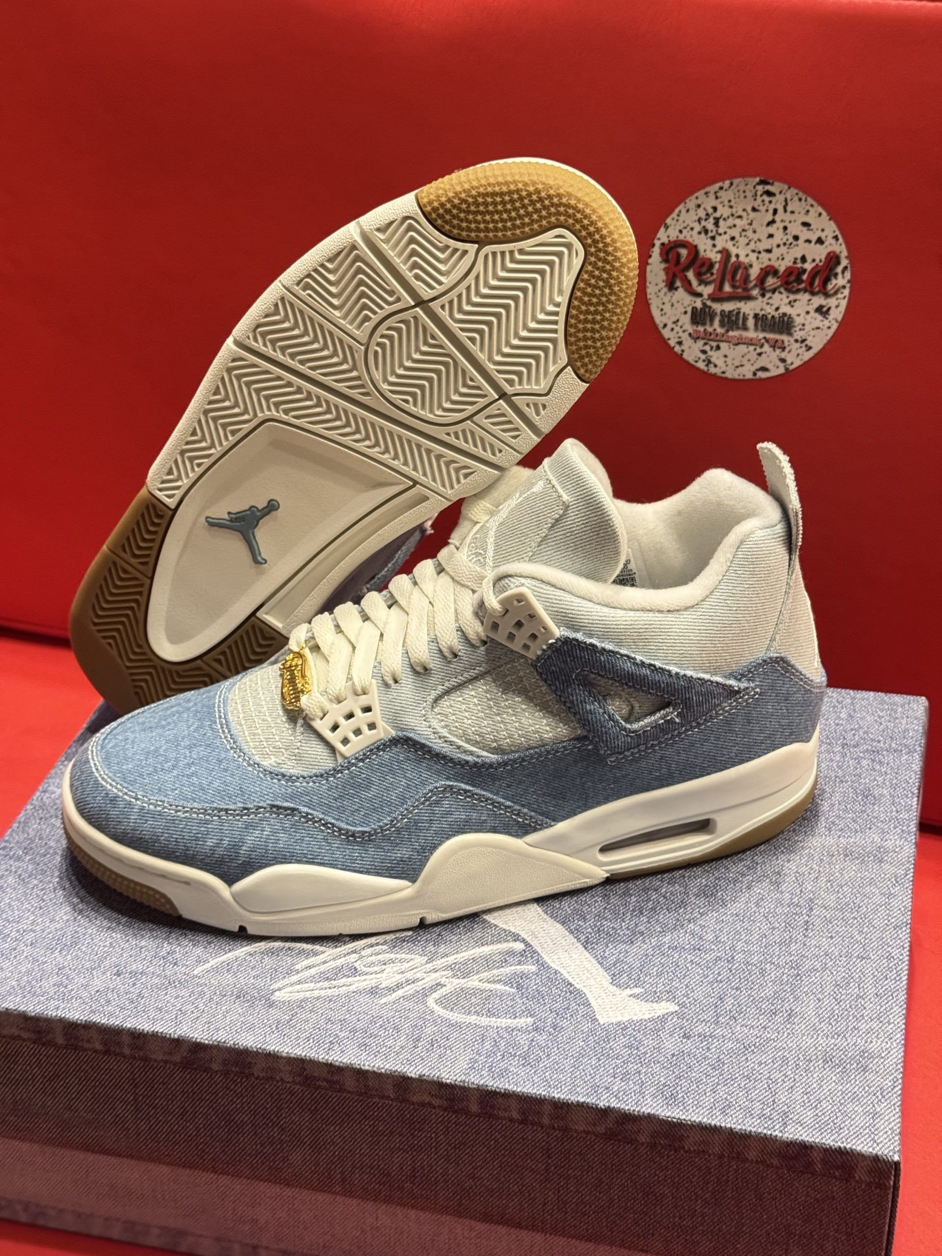 Air Jordan 4 sneakers with denim upper and brown soles, on denim box, against a red background.