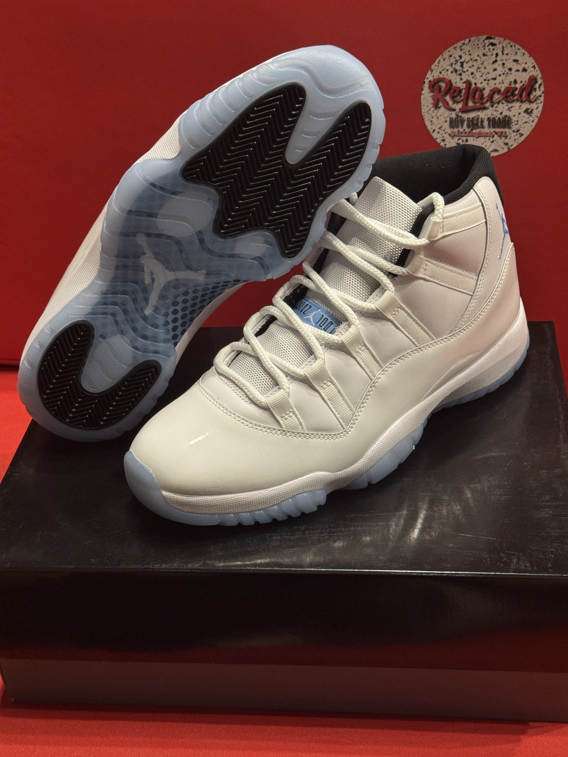 White and light blue Air Jordan 11 sneakers on a black box, set against a red background.