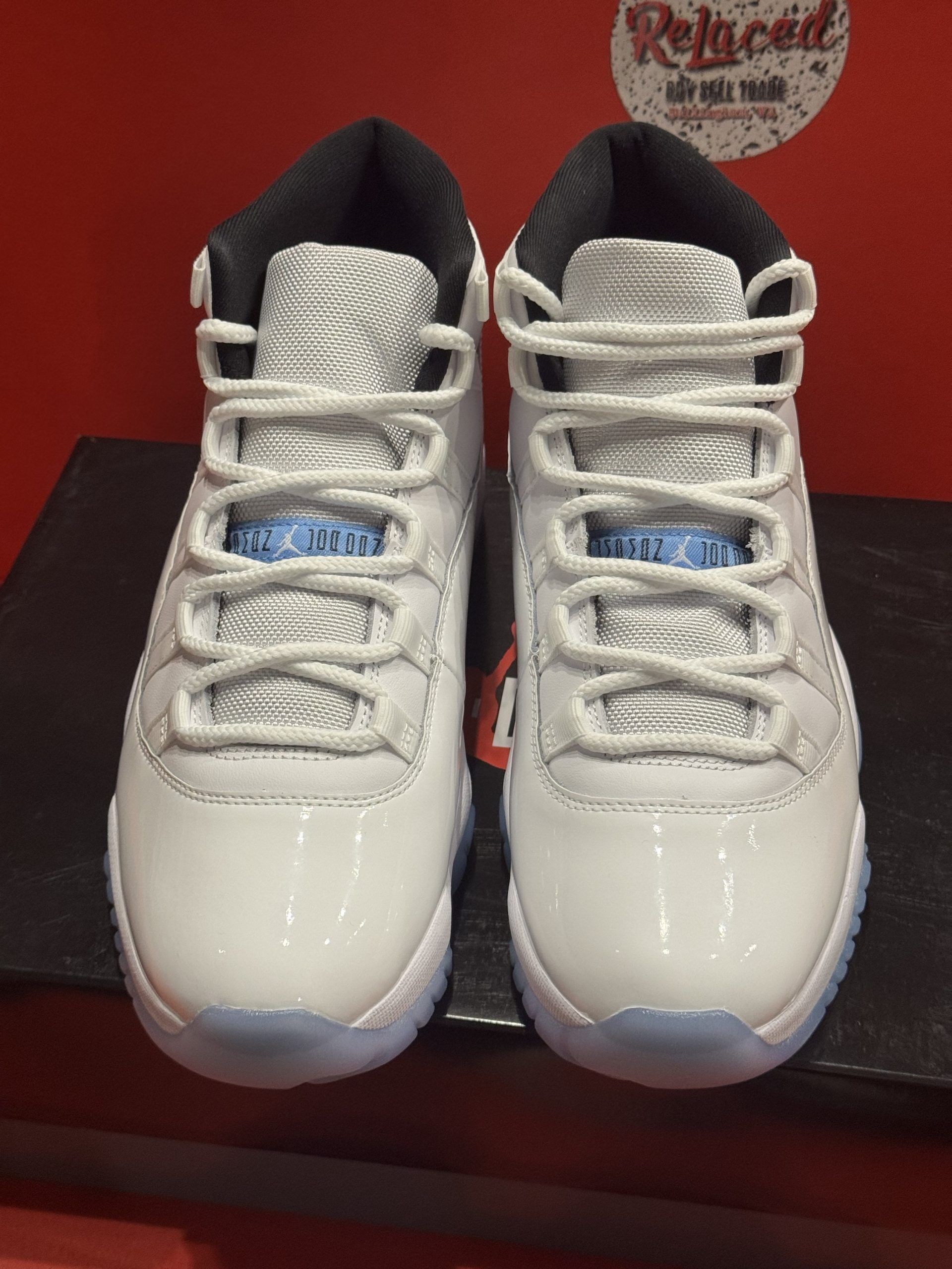 White and light blue Air Jordan 11 sneakers on a black box, set against a red background.