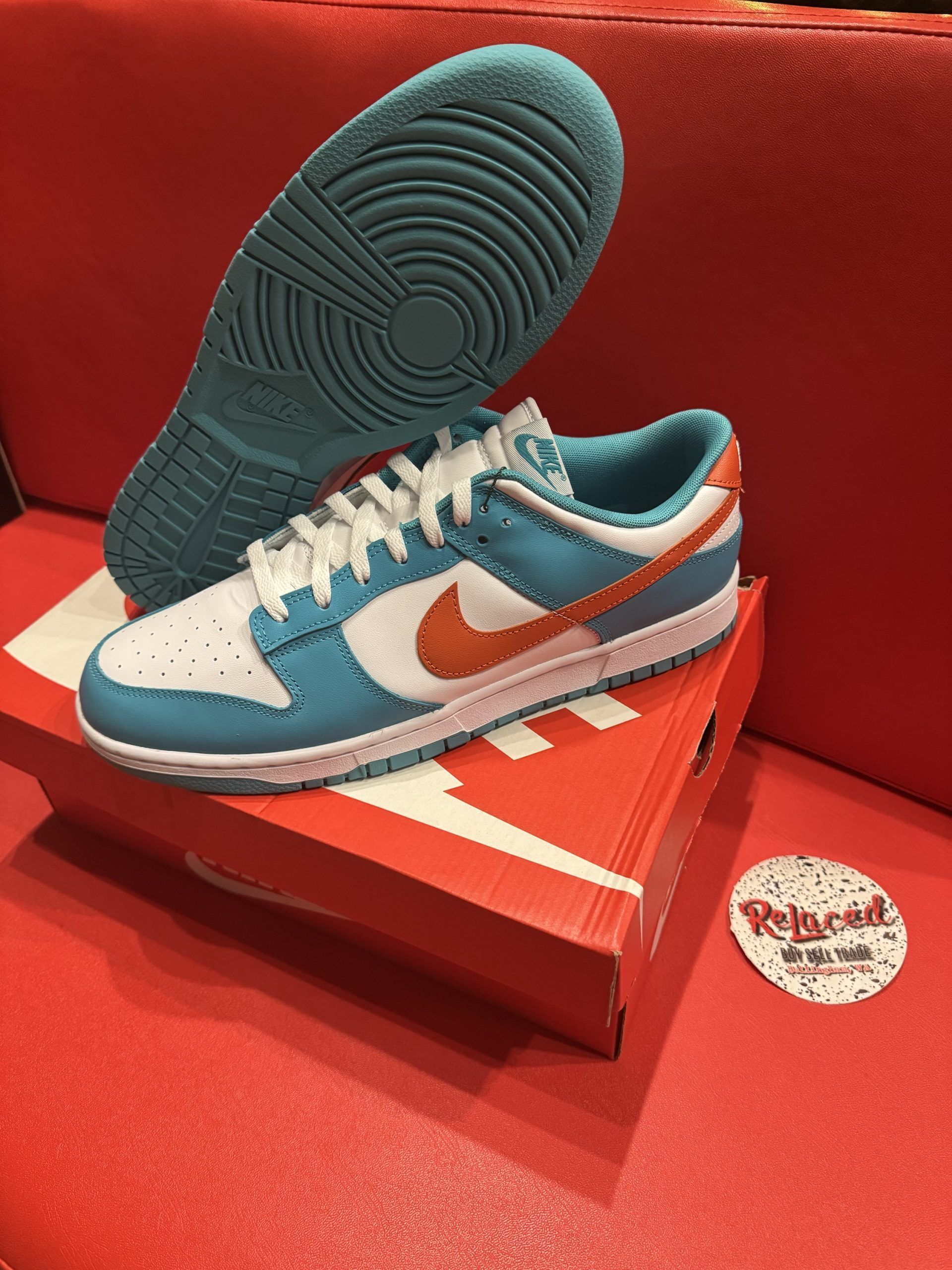 Nike Dunk Low sneakers, blue and white with orange Swoosh, on a red box, red backdrop.