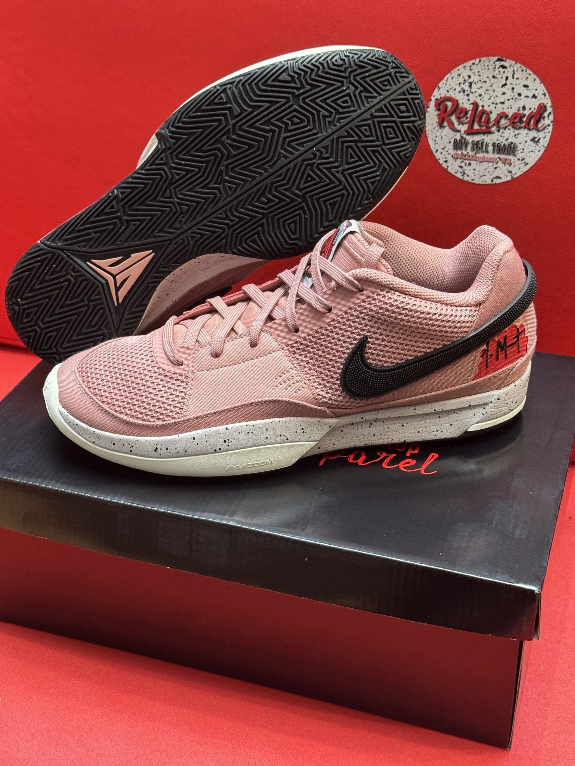 Pink Nike basketball shoe with a black swoosh, sitting on a black box. The sole of the shoe is visible.