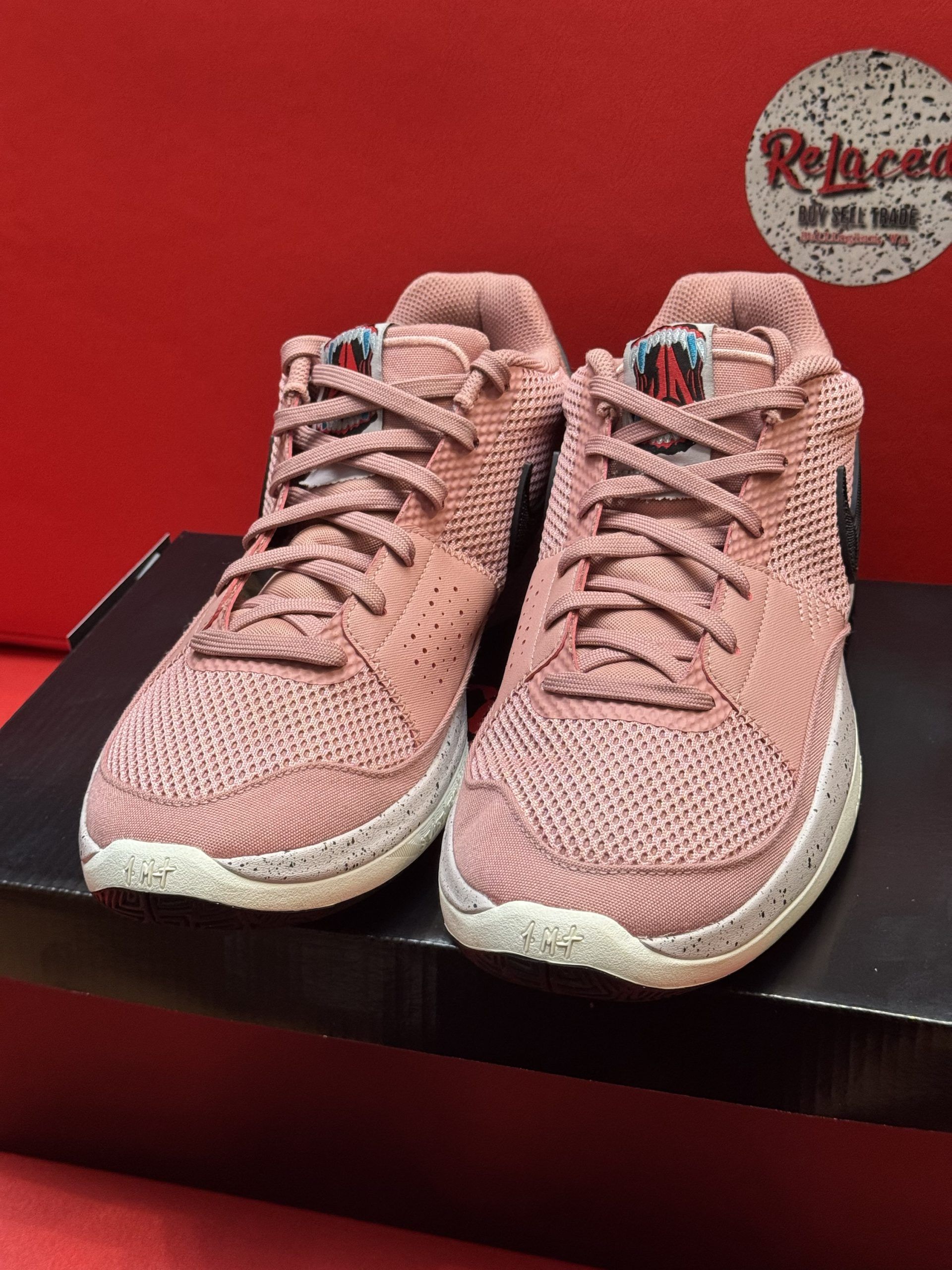 Pink Nike basketball shoe with a black swoosh, sitting on a black box. The sole of the shoe is visible.