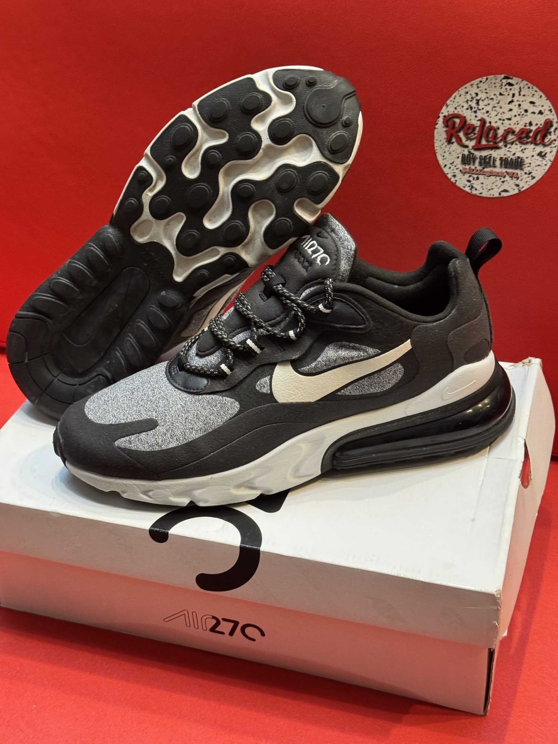 Black and gray Nike Air Max 270 sneakers on a white box, with white swoosh, and a textured black and white sole.