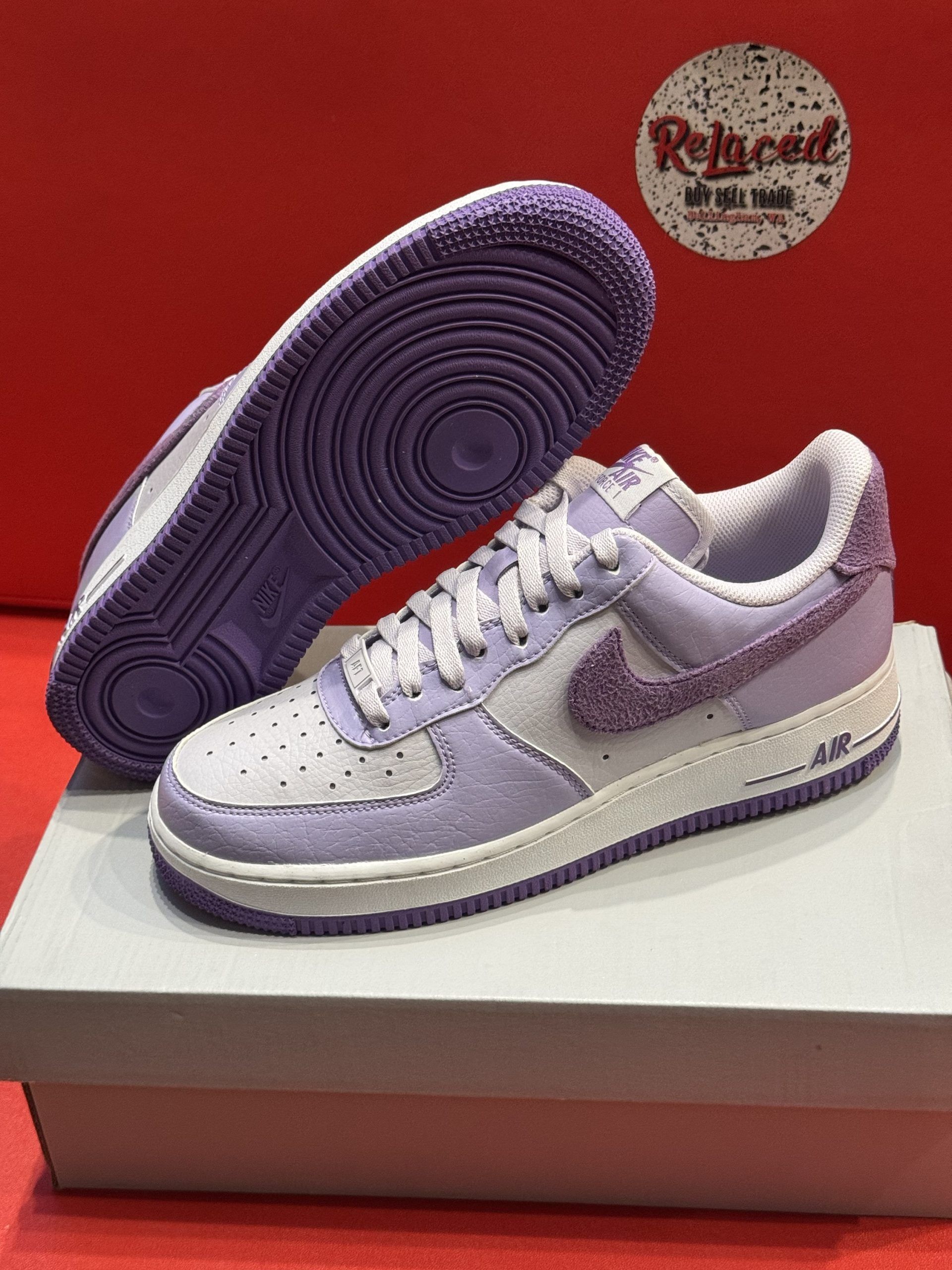 Purple and white Nike Air Force 1 sneakers on a white box, red background.