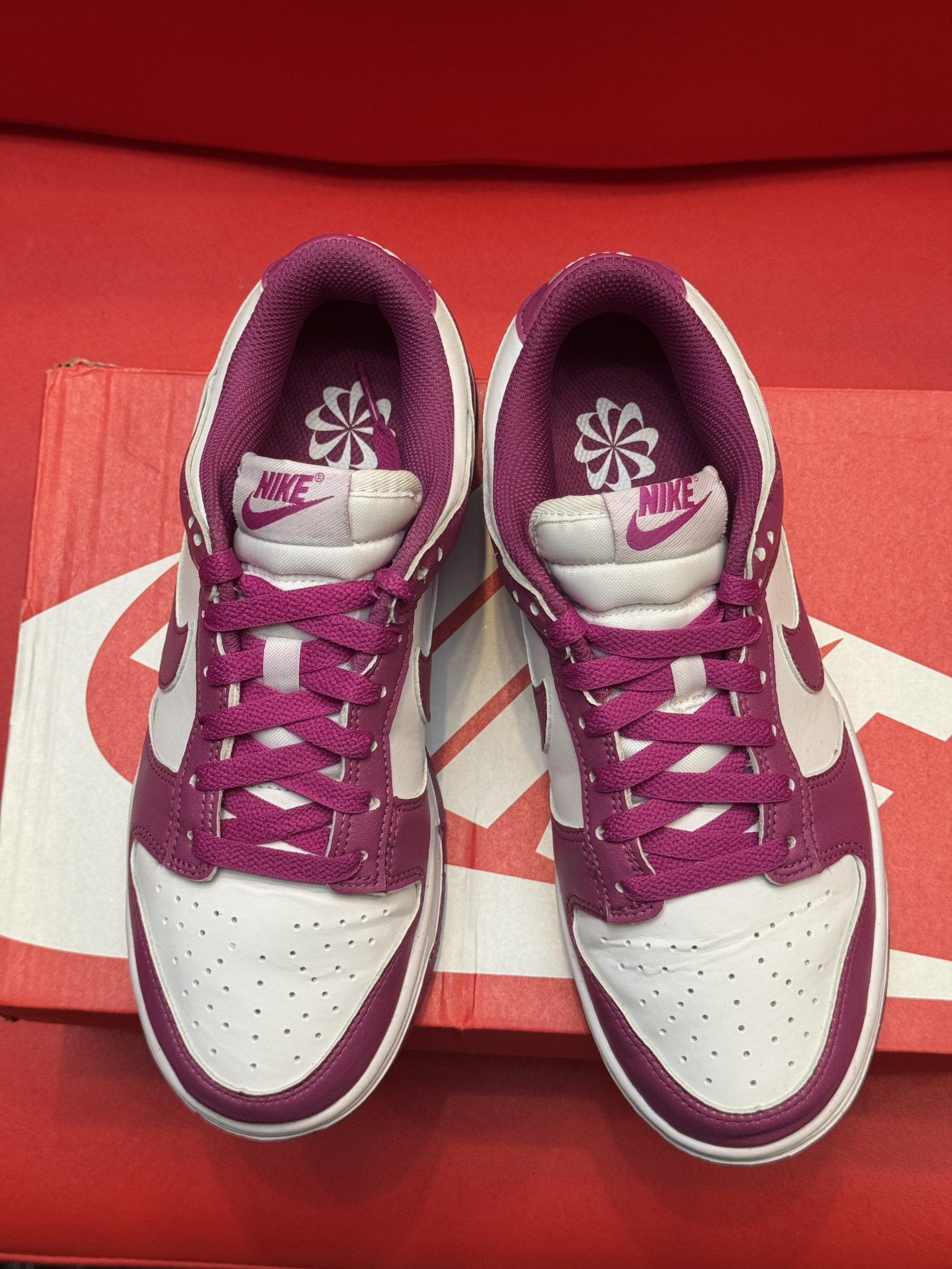 Nike Dunk Low sneakers in white and purple, displayed on a red Nike shoebox.