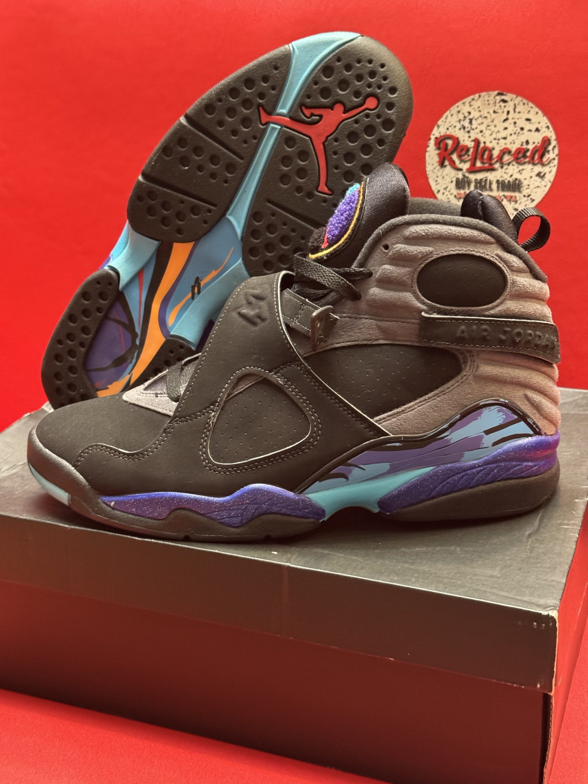Black, teal, and purple Air Jordan 8 sneakers on a box, with a red background.
