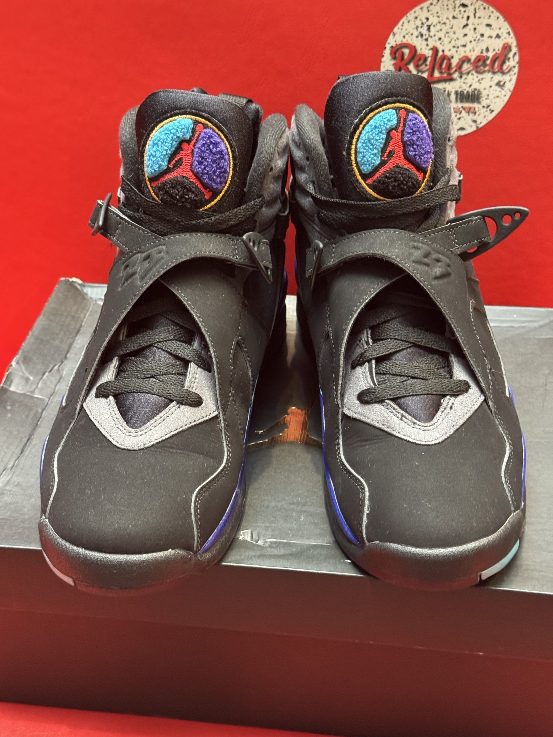 Black, teal, and purple Air Jordan 8 sneakers on a box, with a red background.