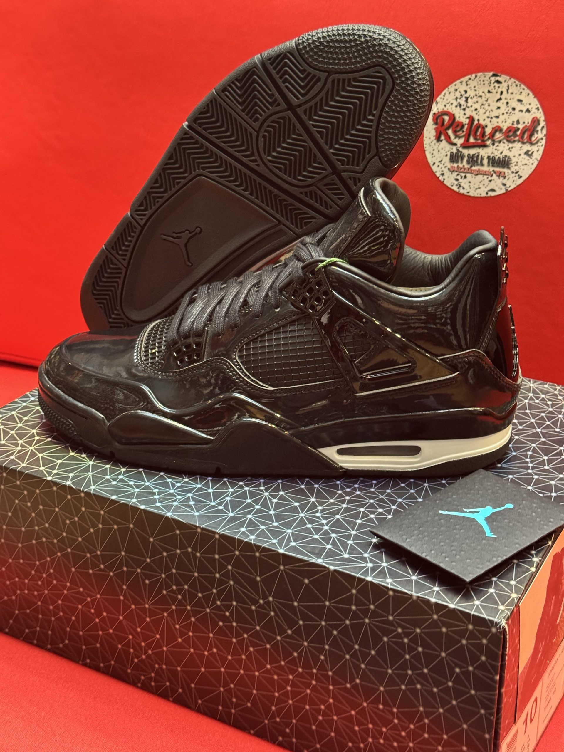 Black Air Jordan 4 sneakers on a box, with a card bearing the Jumpman logo and a red backdrop.