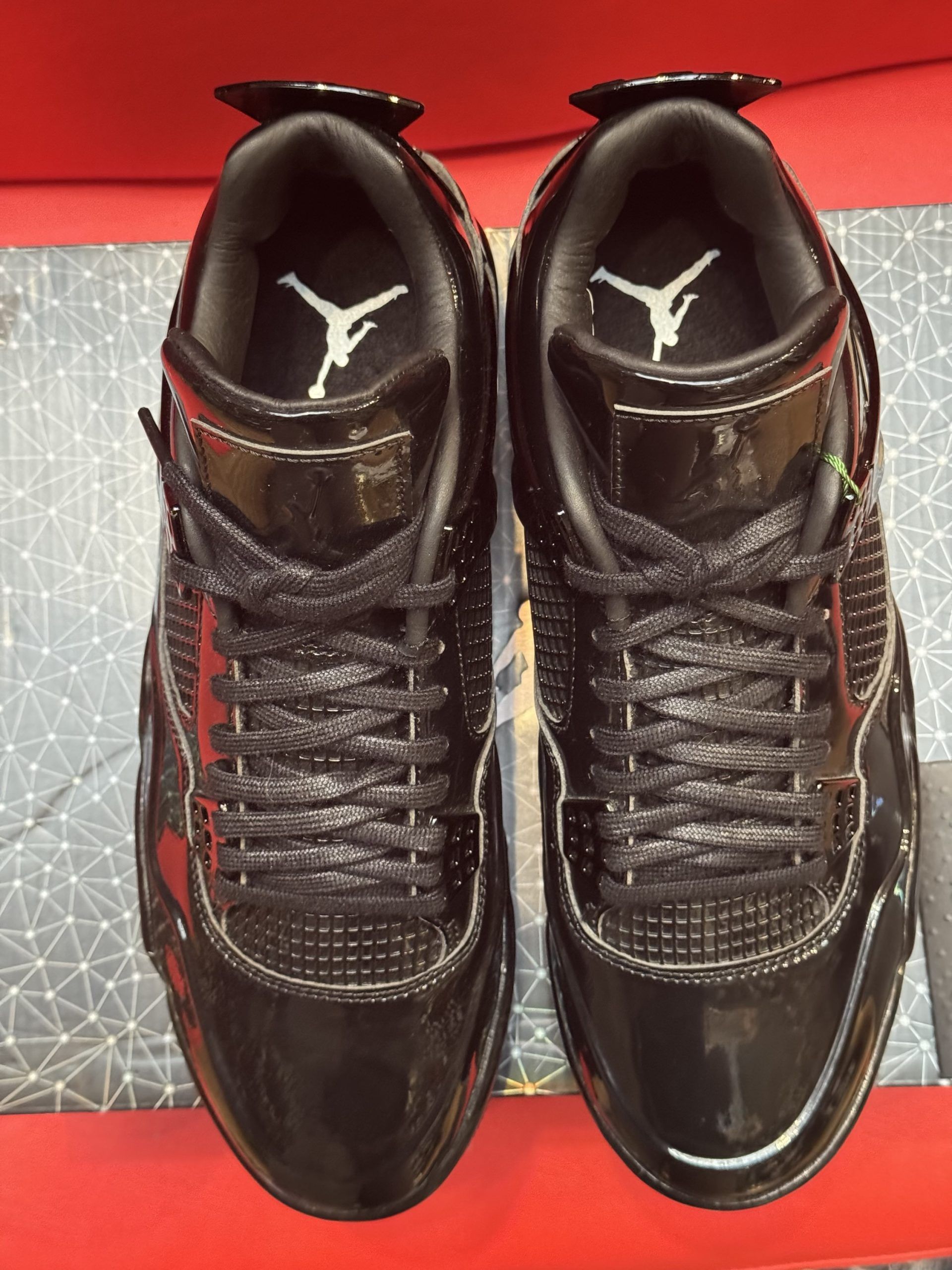 Black Air Jordan 4 sneakers on a box, with a card bearing the Jumpman logo and a red backdrop.