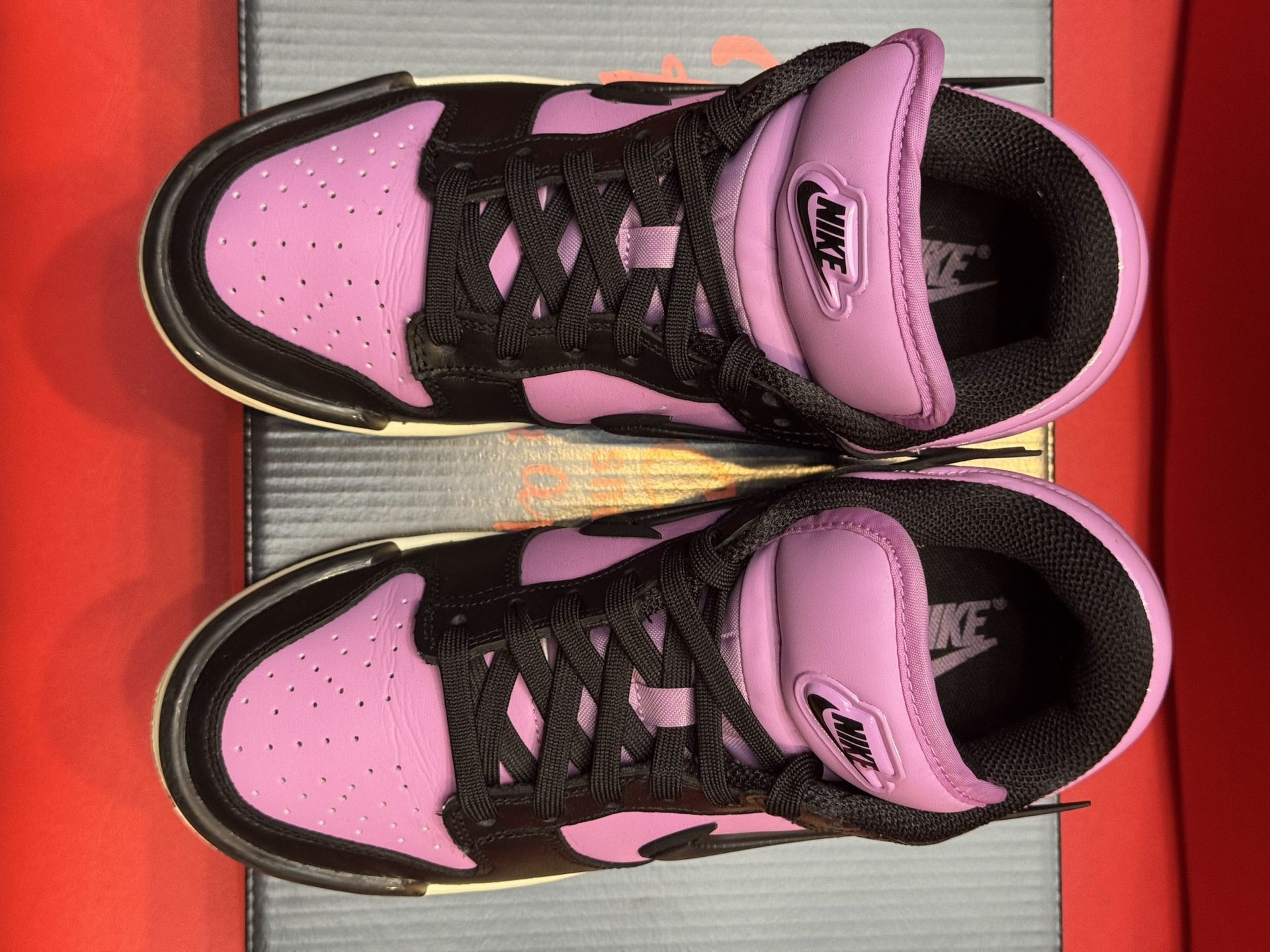 Black and purple Nike Dunk Low sneakers with black sole, resting on a shoebox against a red backdrop.