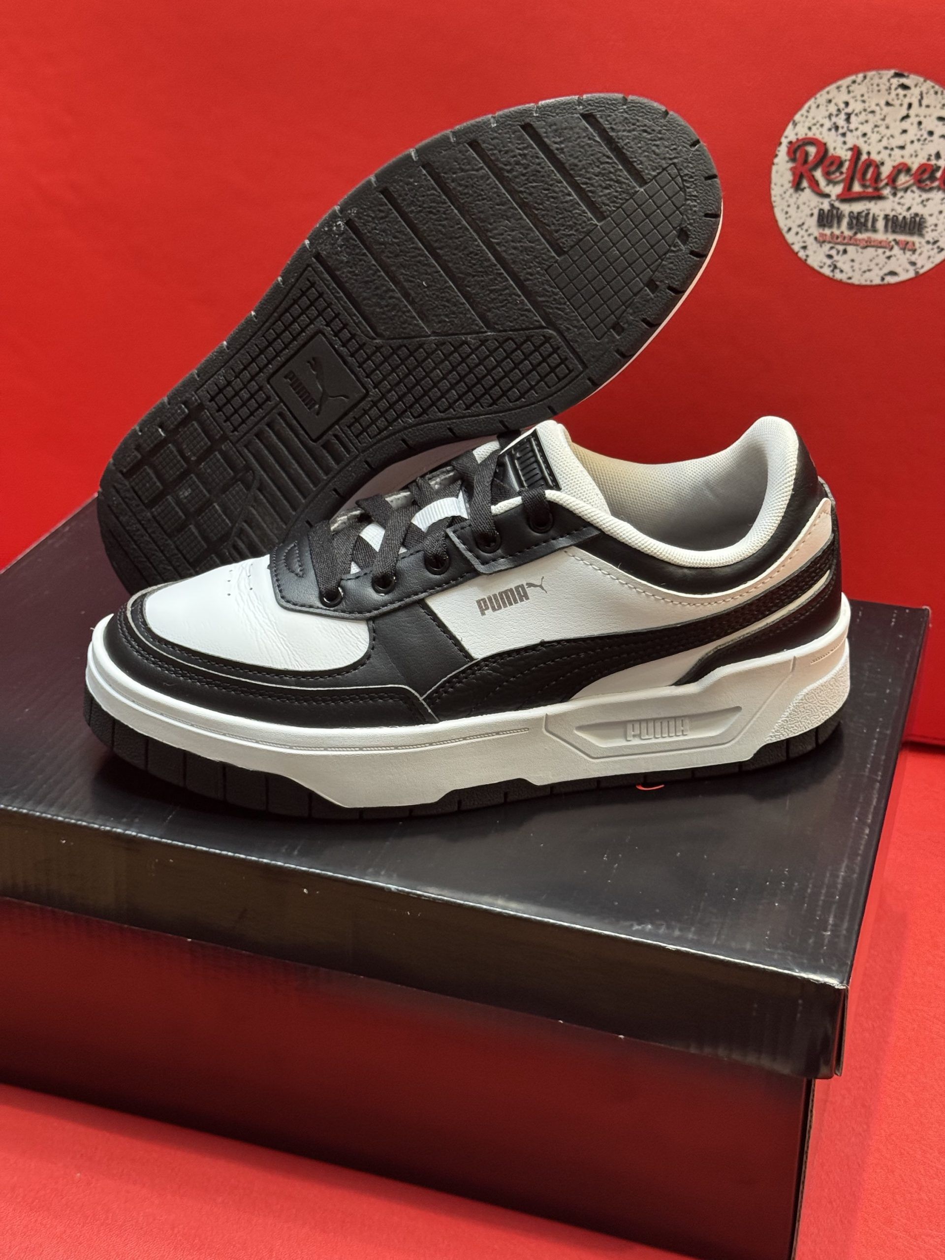 White and black sneakers with black sole, sitting on a black box against a red background.