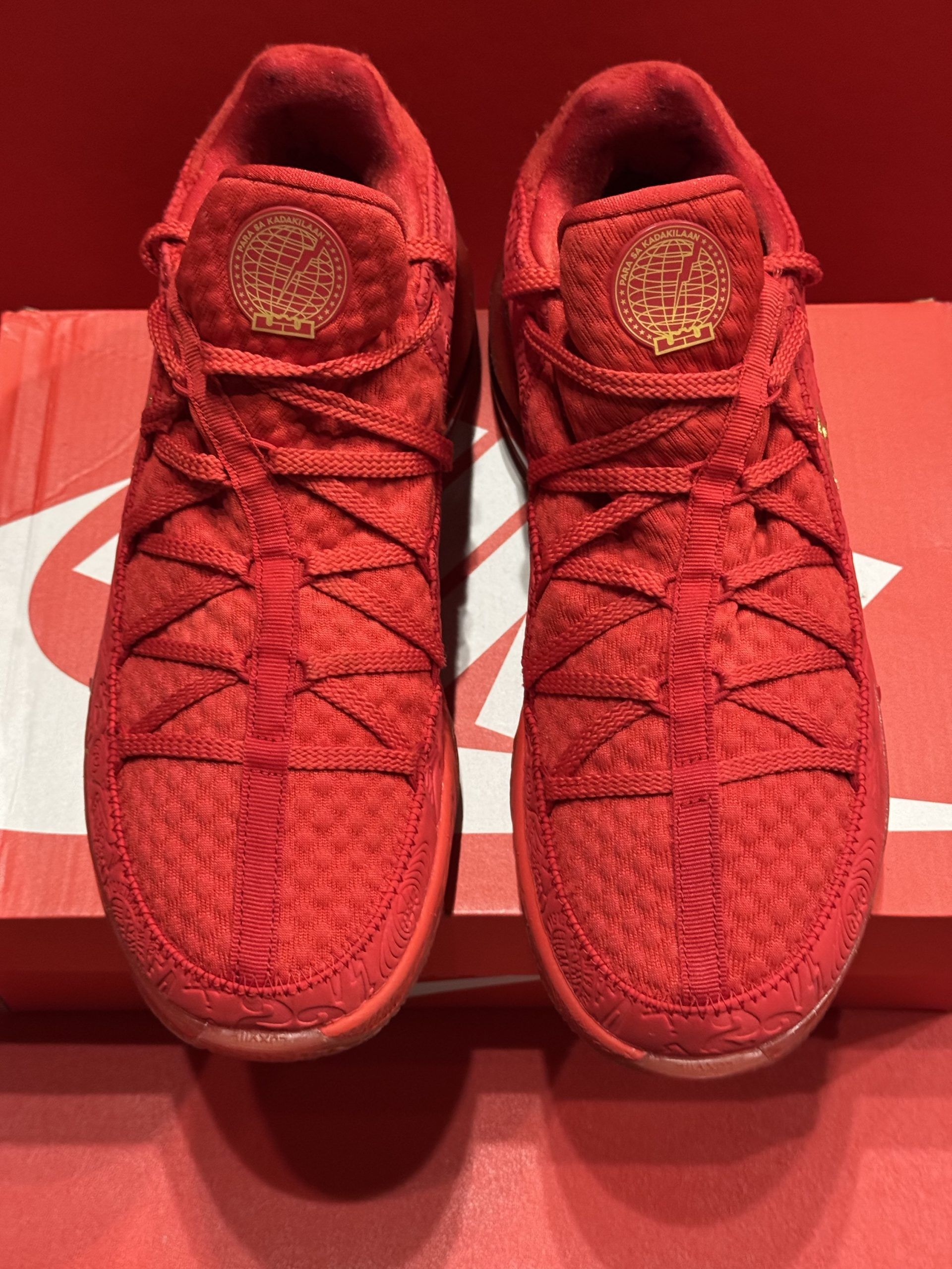 Red Nike LeBron 17 basketball shoe with gold accents on a red box, red background.