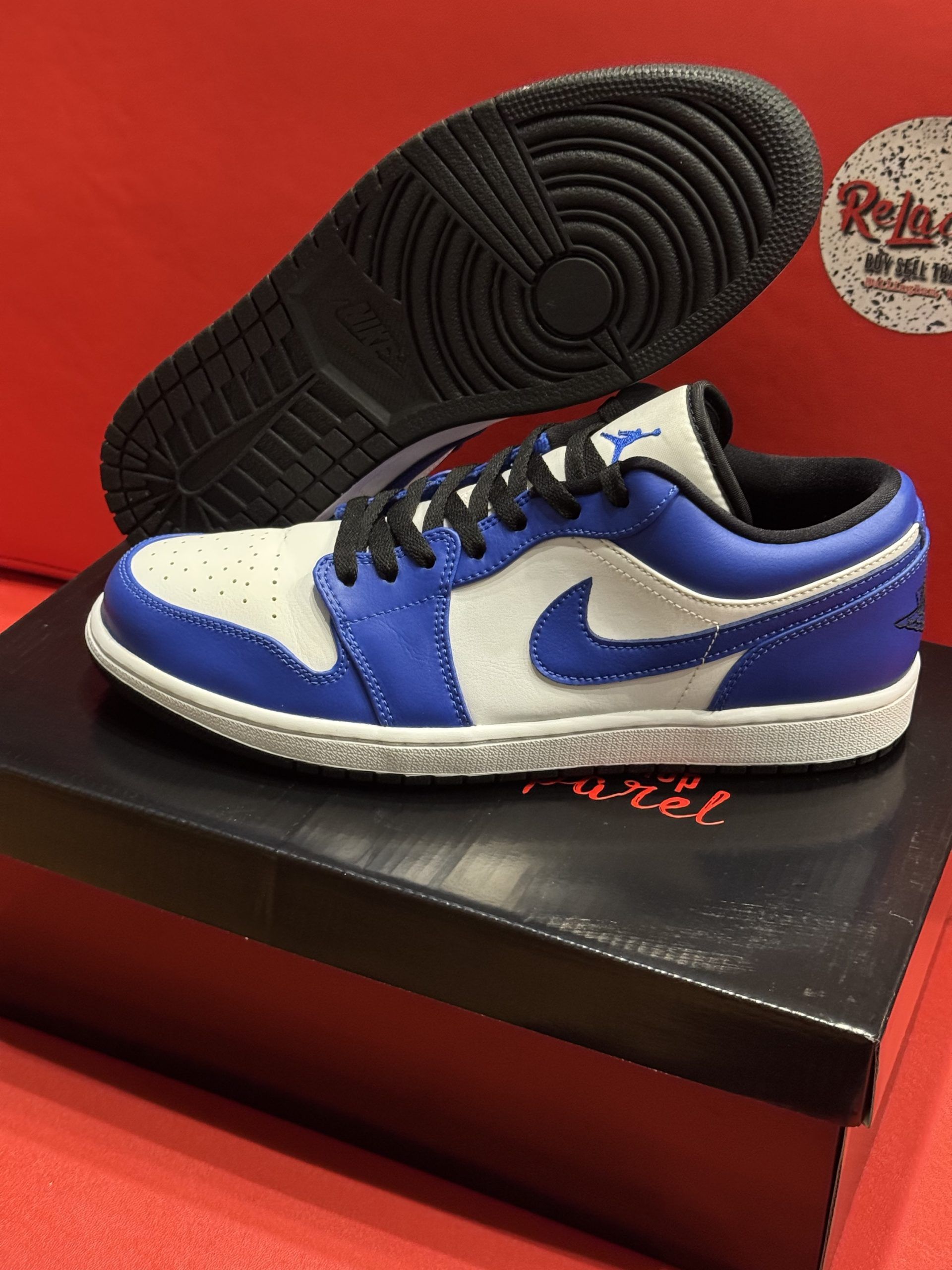 Blue and white Air Jordan 1 Low sneaker on a black box, sole visible.