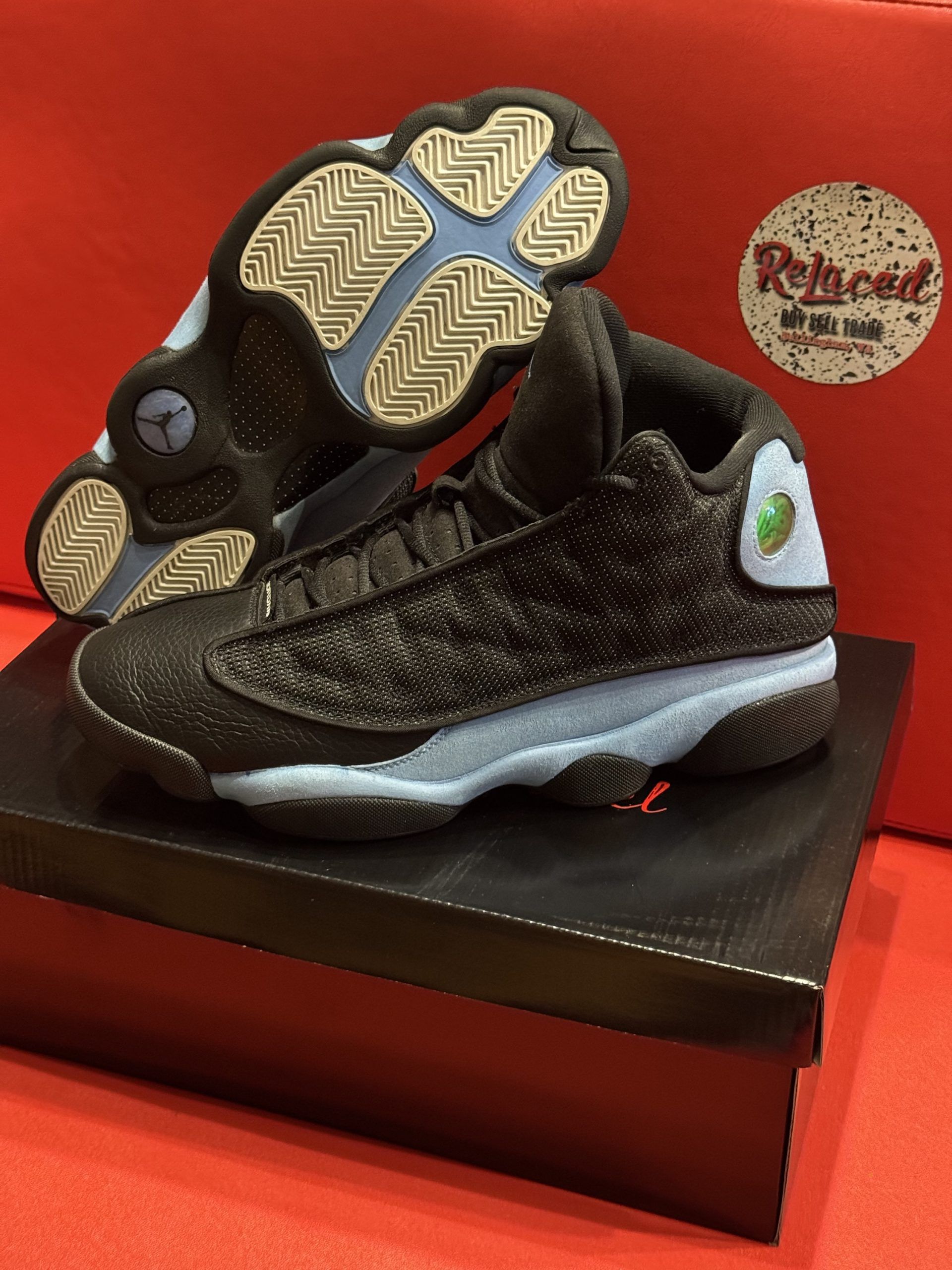 Baby Air Jordan 13 sneakers, black with light blue accents, resting on a black shoebox.