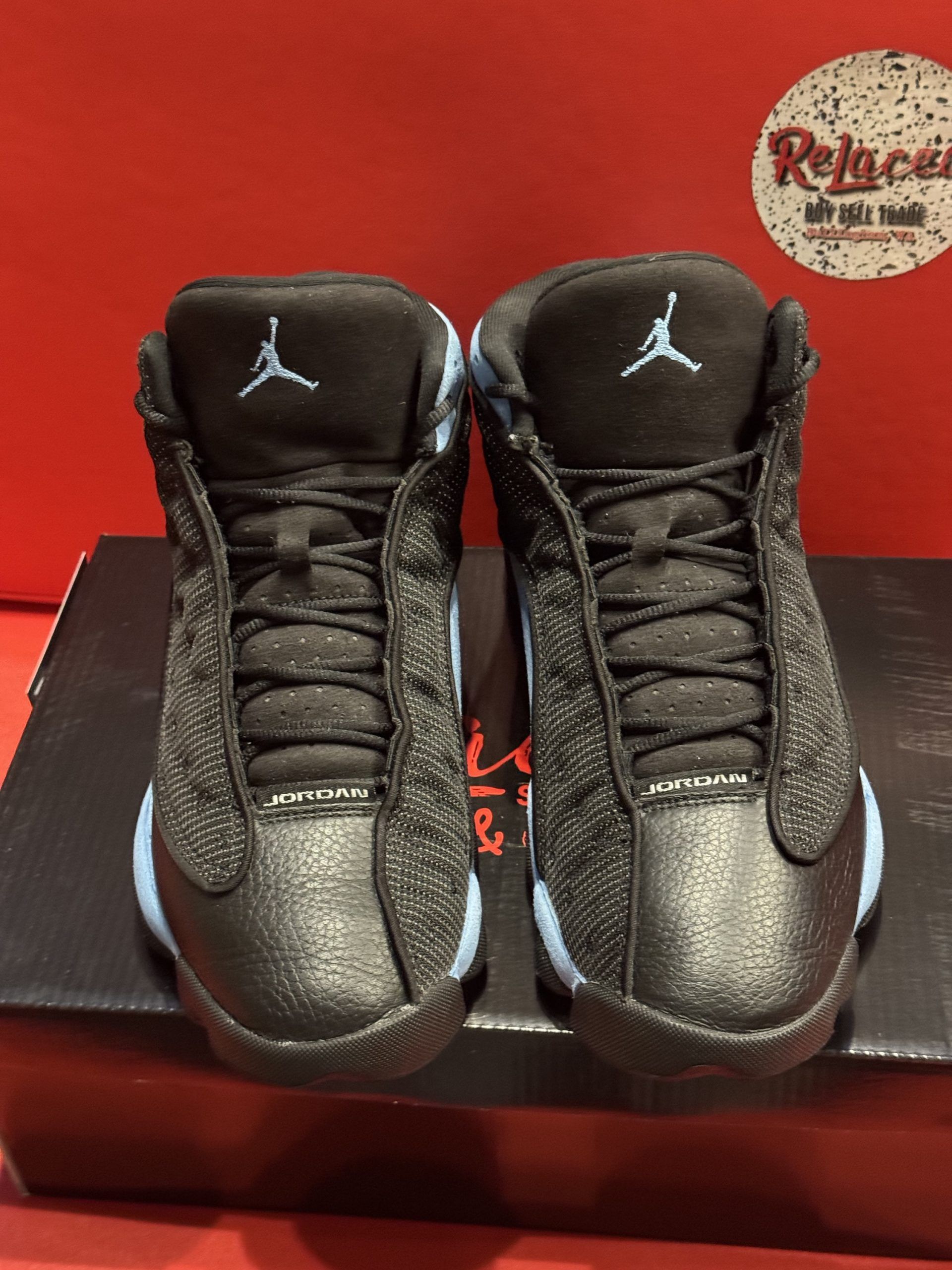 Baby Air Jordan 13 sneakers, black with light blue accents, resting on a black shoebox.