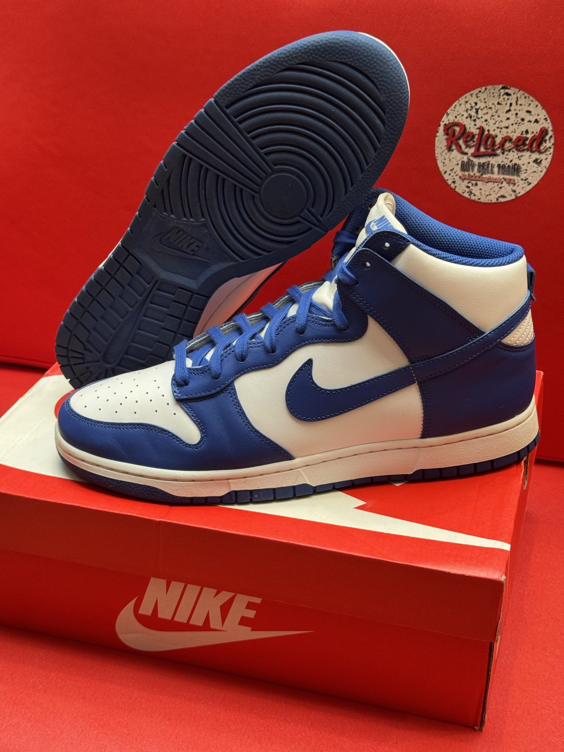 Blue and white Nike Dunk High sneakers displayed on a red Nike box with a matching blue outsole.