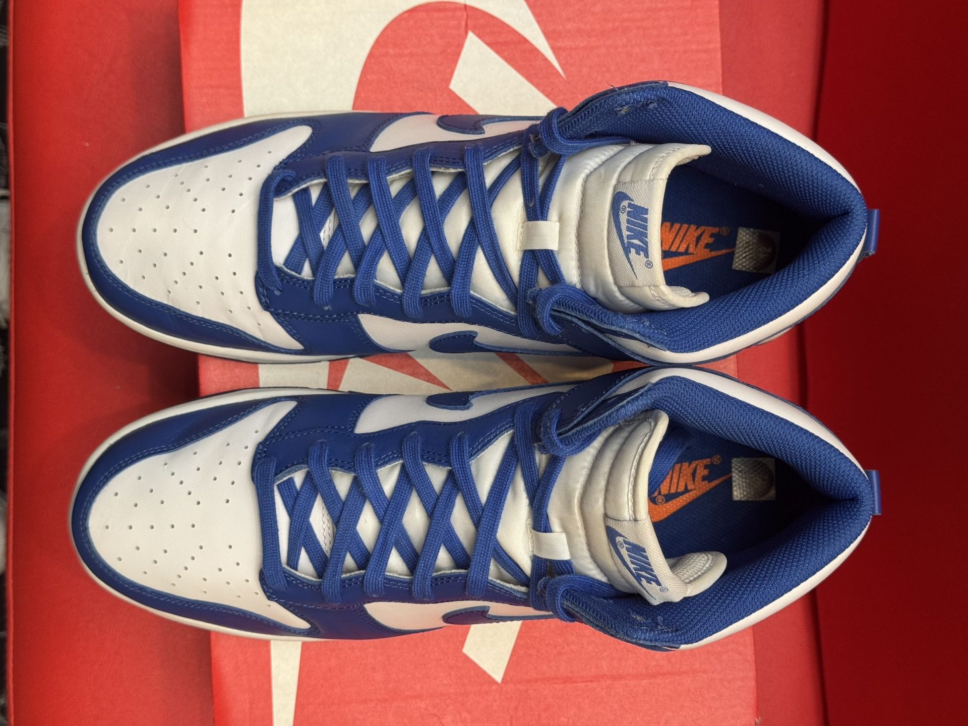 Blue and white Nike Dunk High sneakers displayed on a red Nike box with a matching blue outsole.