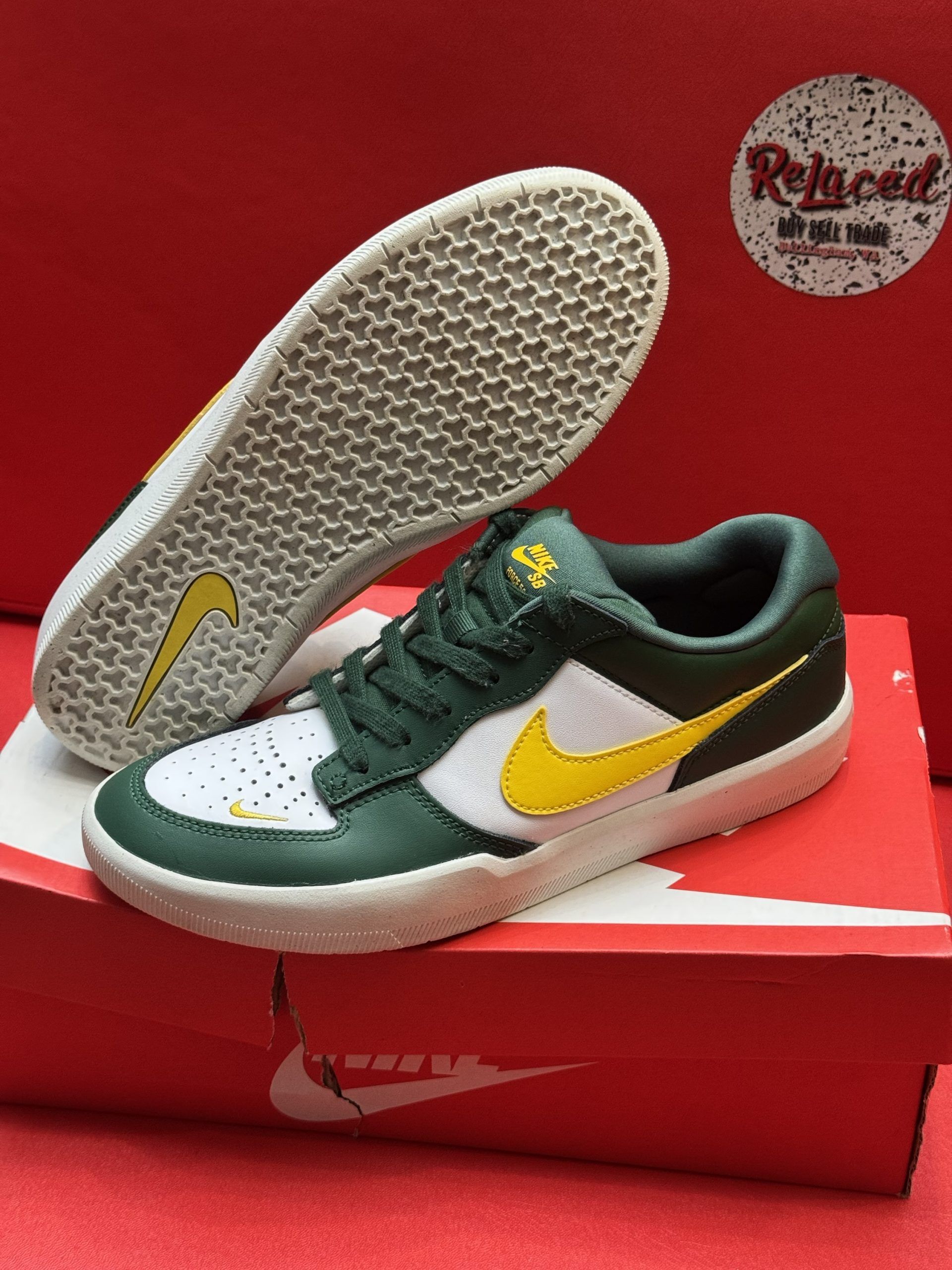 Green and white Nike SB shoes with yellow swoosh, resting on a red Nike box with a sole view on top.
