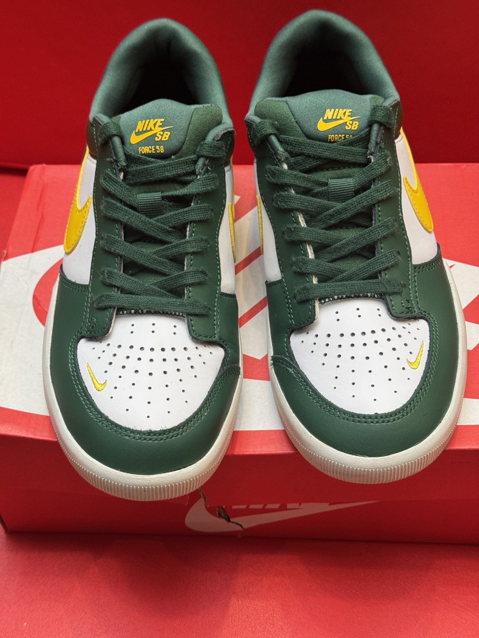 Green and white Nike SB shoes with yellow swoosh, resting on a red Nike box with a sole view on top.