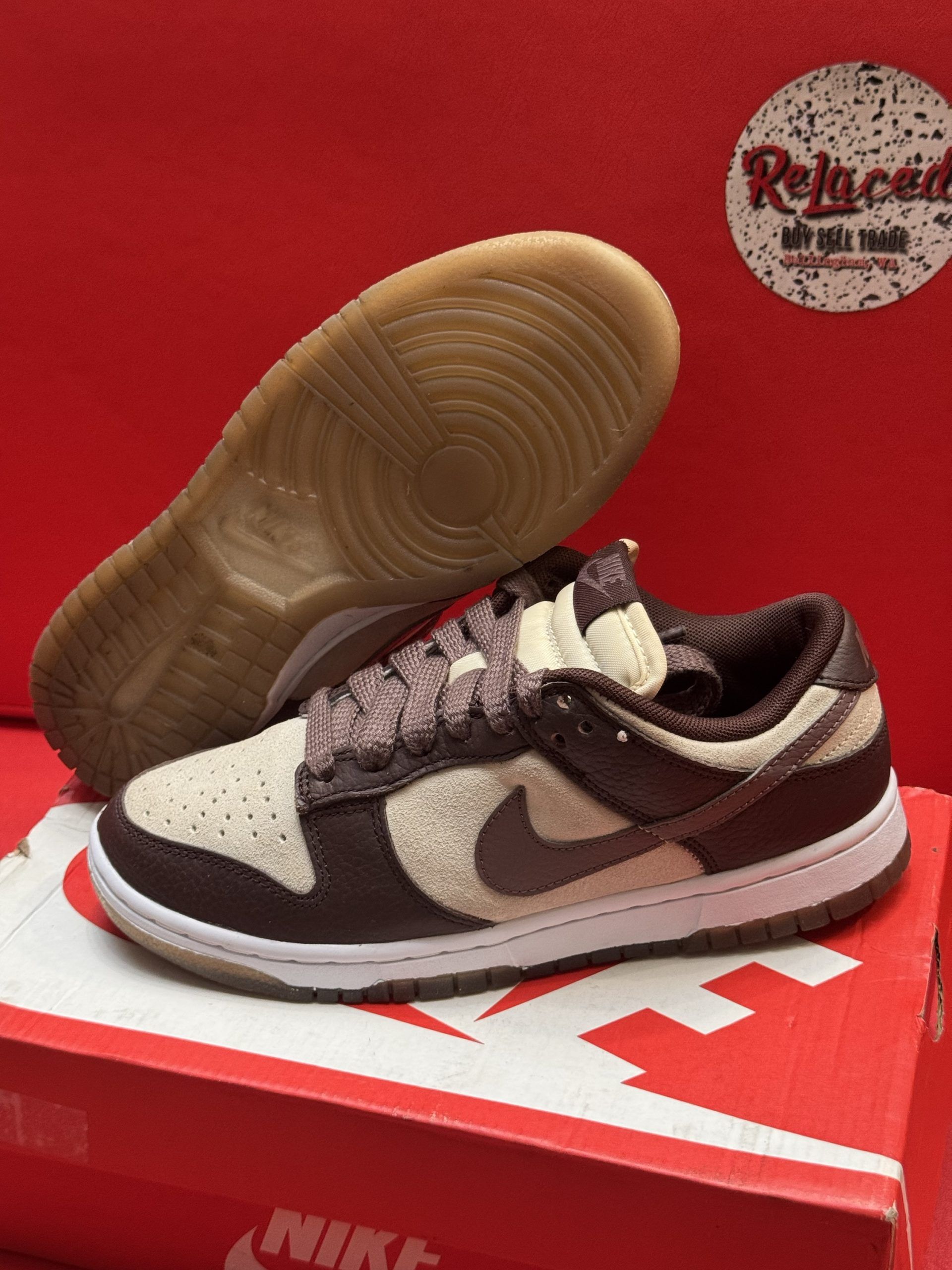 Nike Dunk Low sneakers with brown and tan suede panels, on a red shoebox.