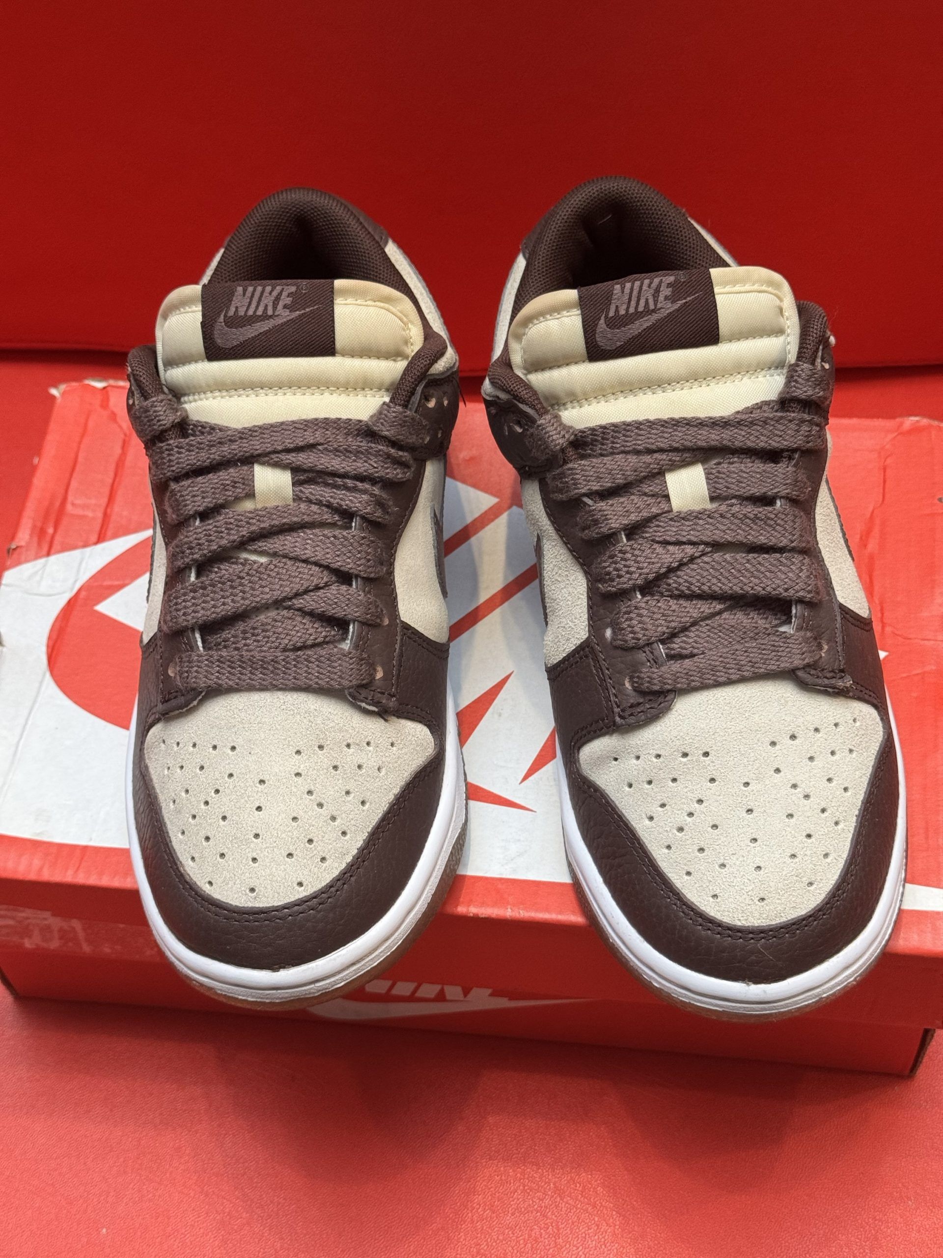 Nike Dunk Low sneakers with brown and tan suede panels, on a red shoebox.