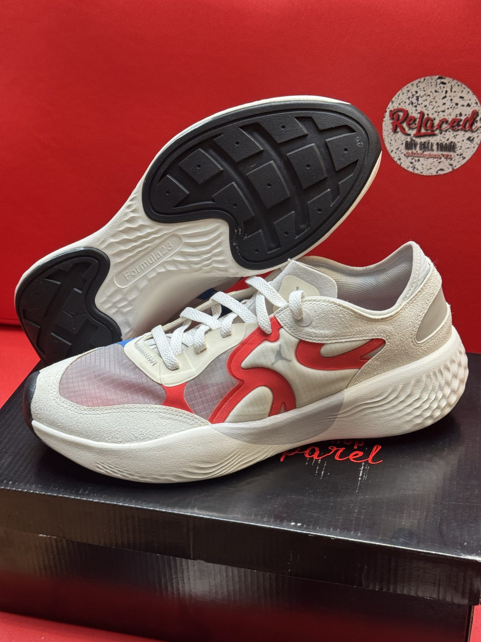 White and red athletic shoe on a black box, sole visible, against a red backdrop.