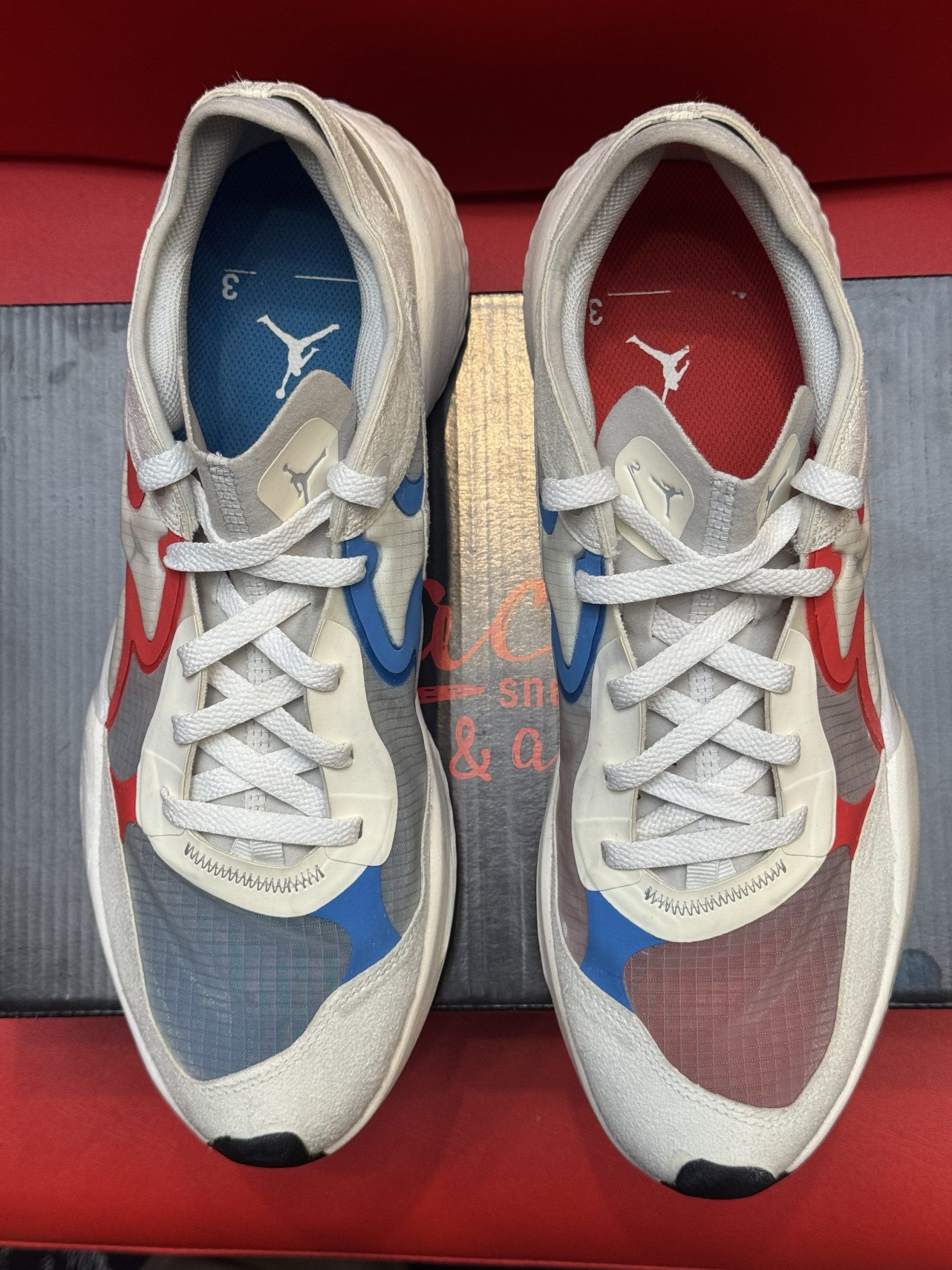 White and red athletic shoe on a black box, sole visible, against a red backdrop.