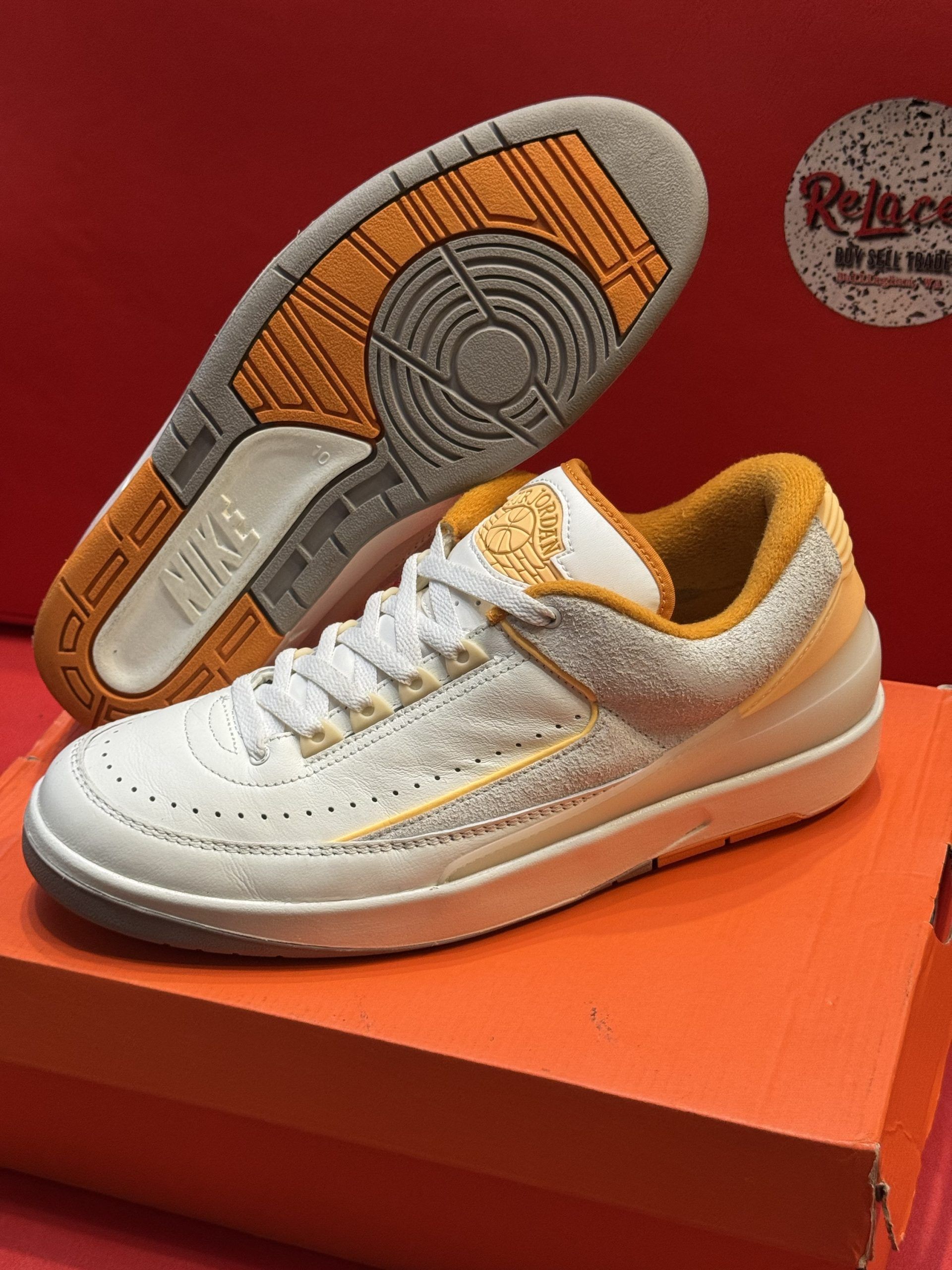 White and yellow Nike sneakers with orange sole and lining, on a box.