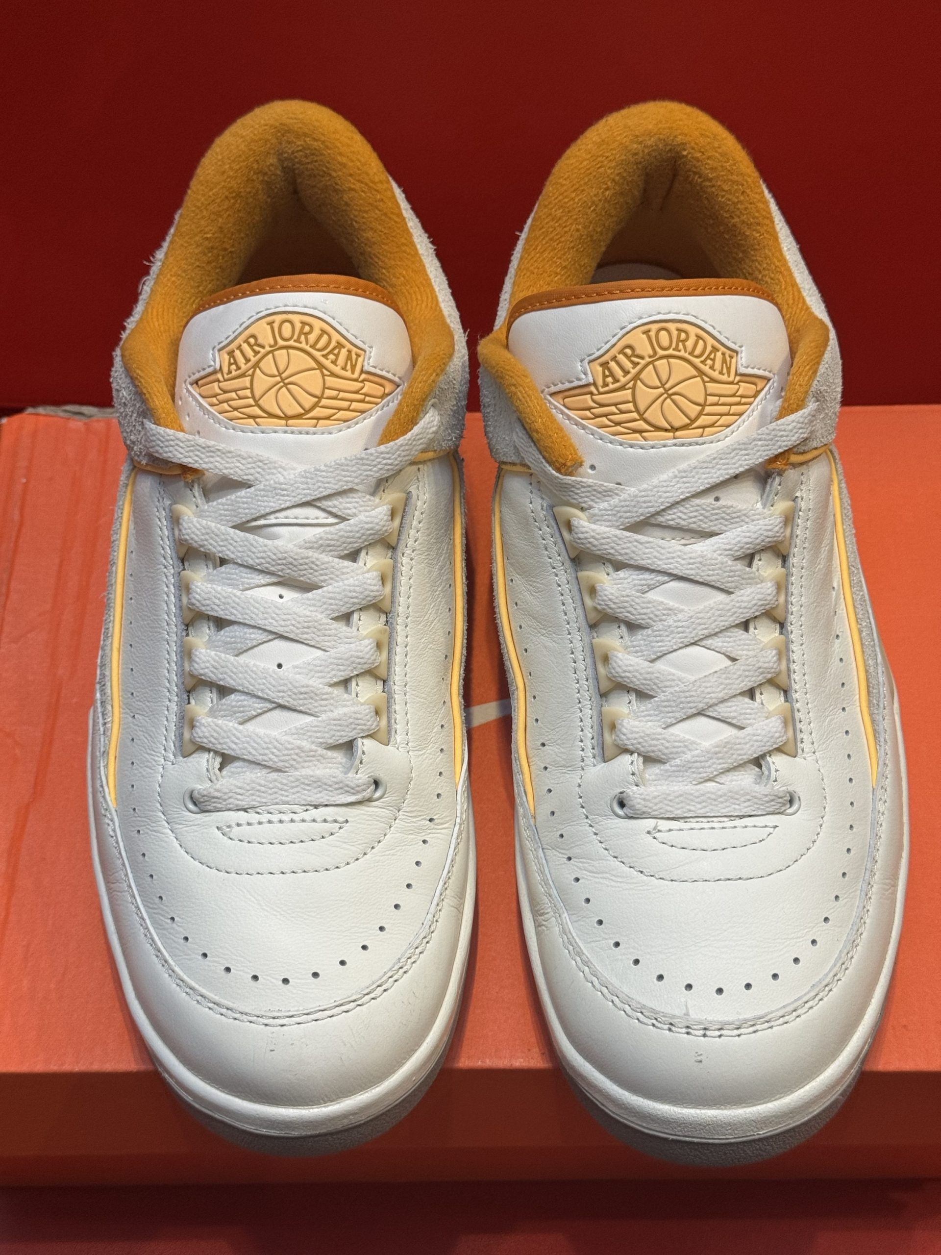 White and yellow Nike sneakers with orange sole and lining, on a box.