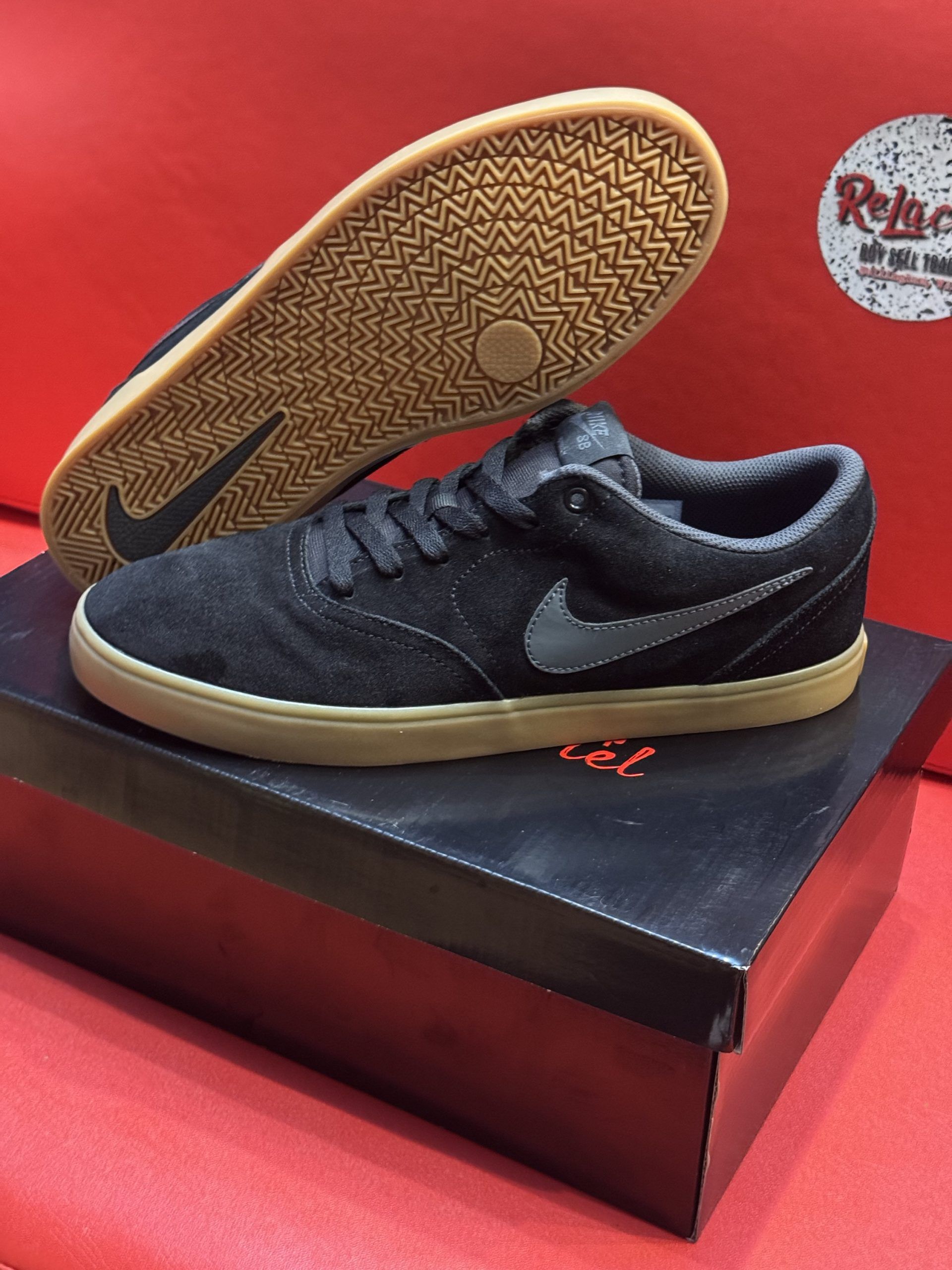 Black Nike sneakers with a gum sole, sitting on a black shoebox, with a red background.